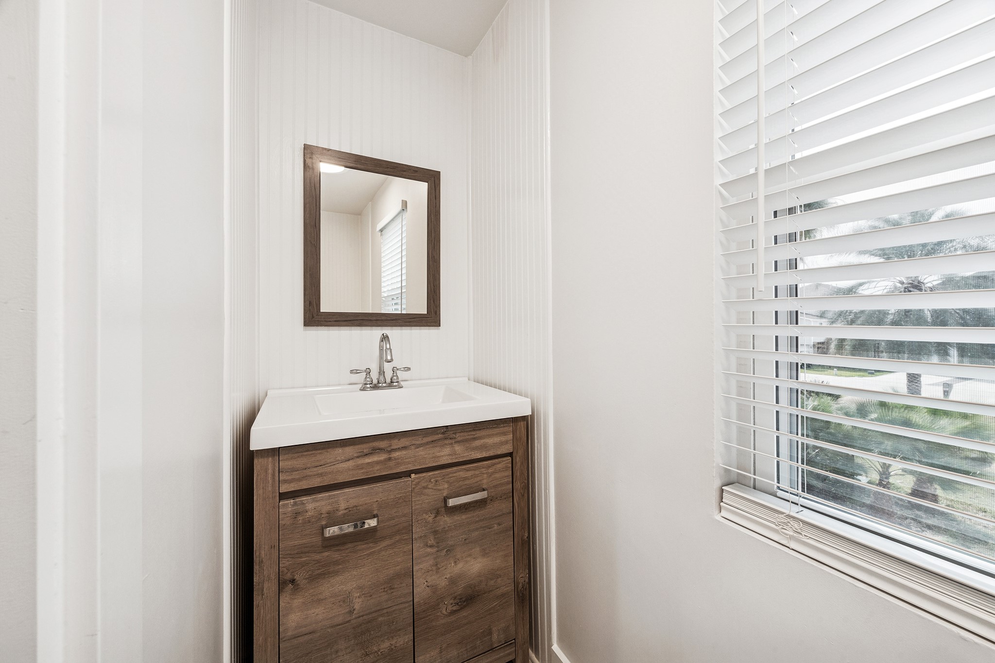 This inviting 1/2 bath powder room boasts a sleek vanity with warm wood accents and a bright window, perfect for welcoming guests with style.