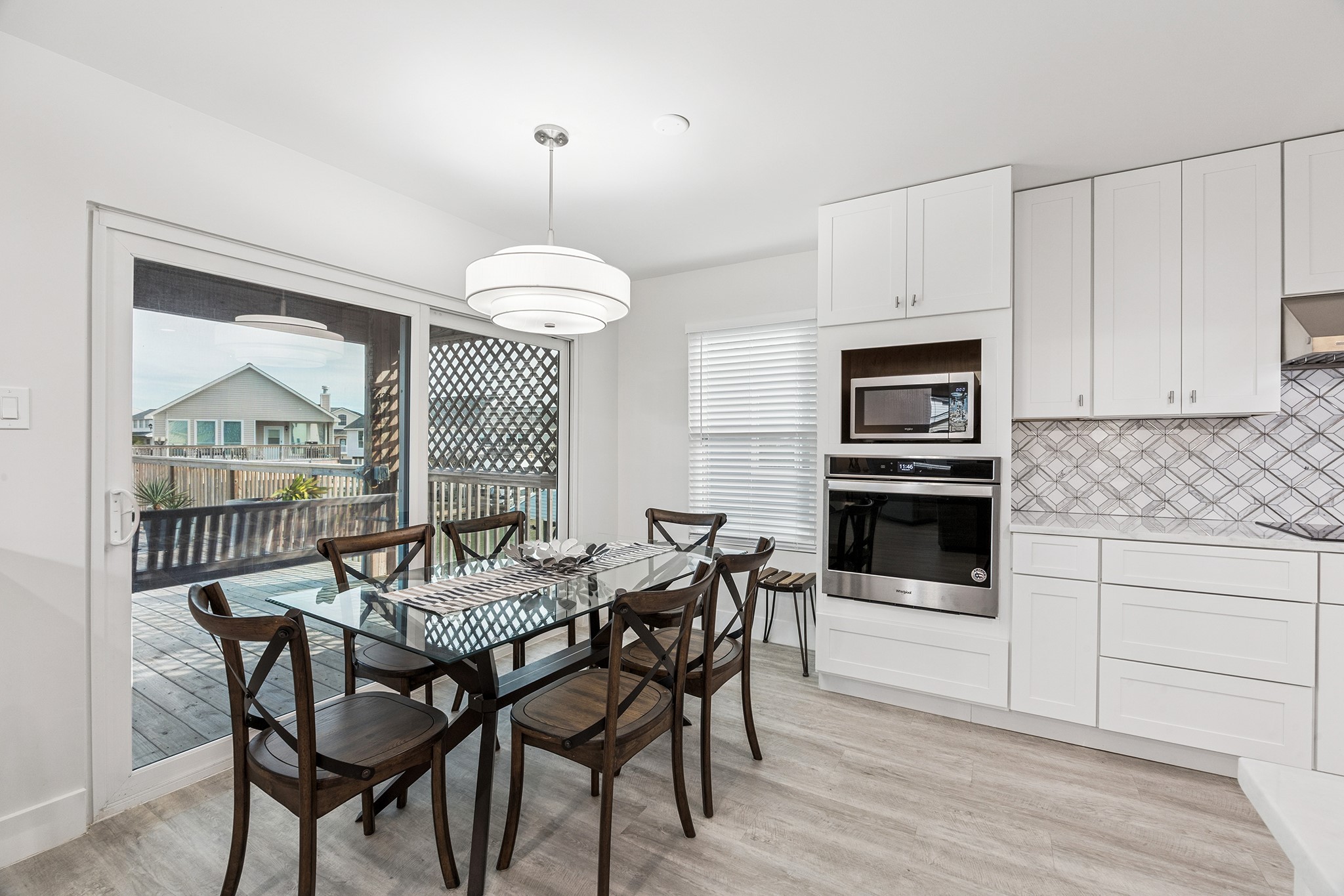 Discover a bright and inviting dining space seamlessly connected to a modern kitchen, featuring elegant cabinetry and an expansive glass door opening to a serene backyard deck, perfect for entertaining and family gatherings.
