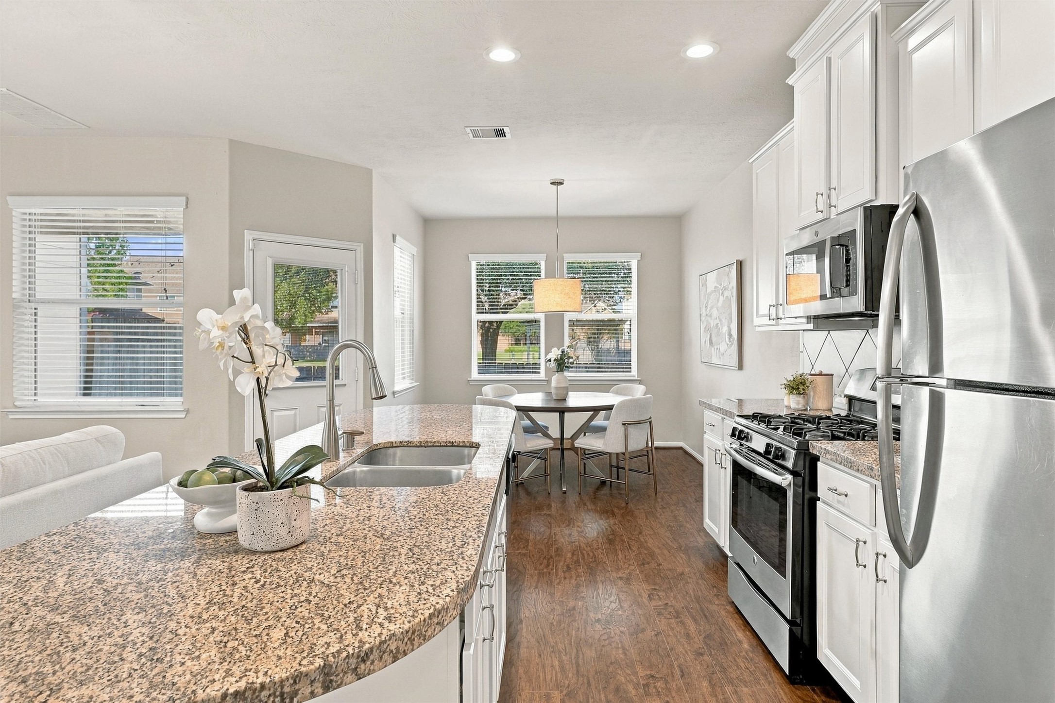 This view of the kitchen shows off the gorgeous natural light that flows through the space.  Wood laminate floors, Sherwin Williams paint, white cabinets, recessed lighting, and an elegant drum shade pendant in the dining room all create a luxurious feel.
