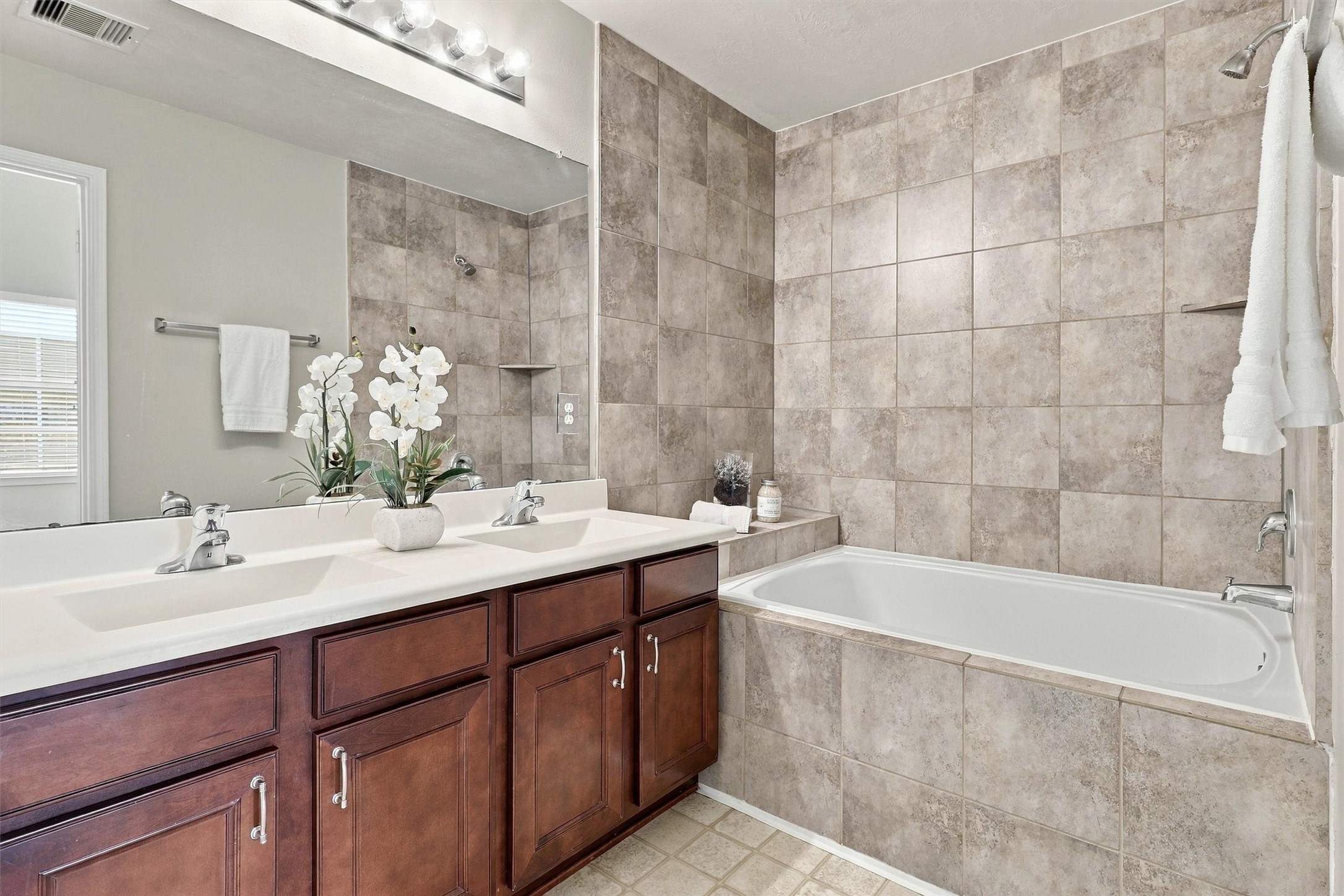 Step through the double doors to find your primary bathroom!  This space features a dual vanity with plenty of storage. Two sinks will make getting ready in the morning a breeze.  the tub/shower combo features a deep garden tub and elevated tile-surround.