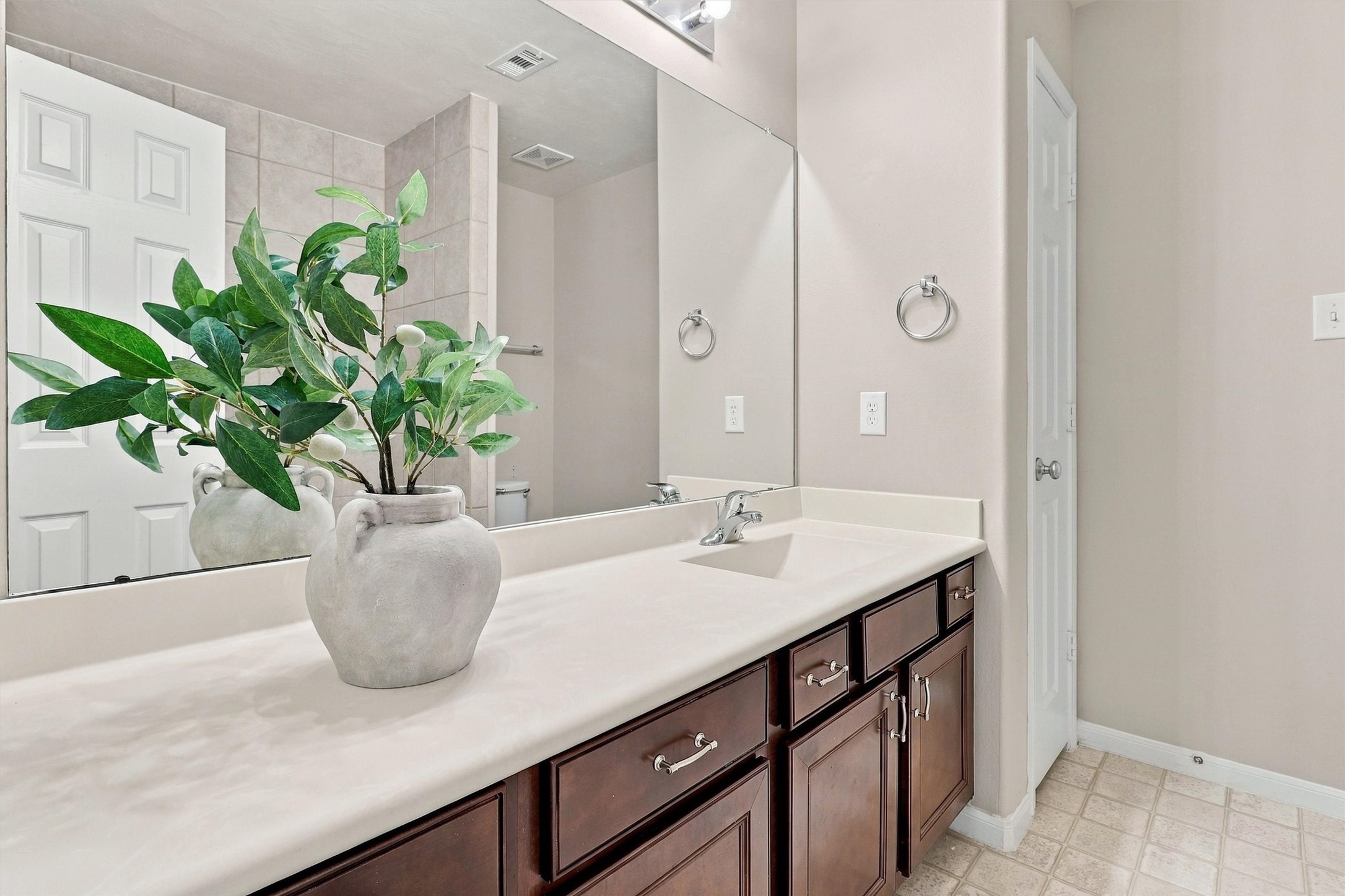 The secondary bath features a long vanity with a single sink.  An elegant composite counter beautifully contrasts the rich stain on the cabinetry.  Note even more storage is available in the linen closet.  The commode is tucked behind the shower wall for privacy.