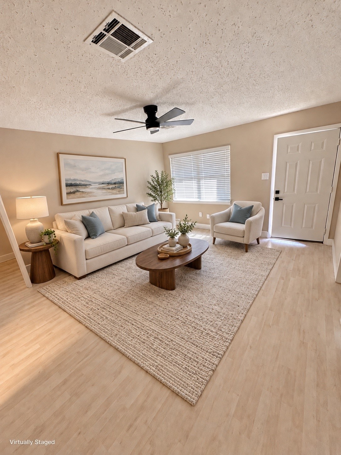 Bright and inviting living room featuring a cozy beige sofa, modern ceiling fan, and large window for natural light, all complemented by a soft area rug and tasteful decor.