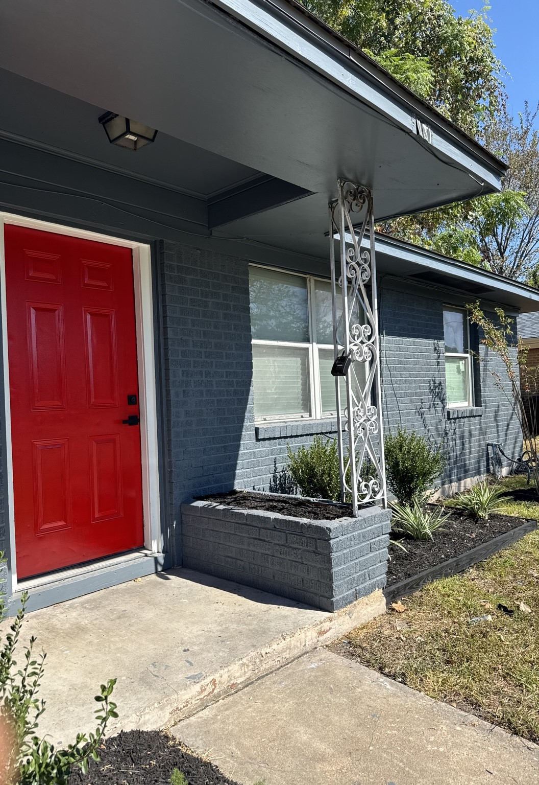 Charming home with a striking red door, complemented by a stylish gray brick exterior and classic decorative ironwork.