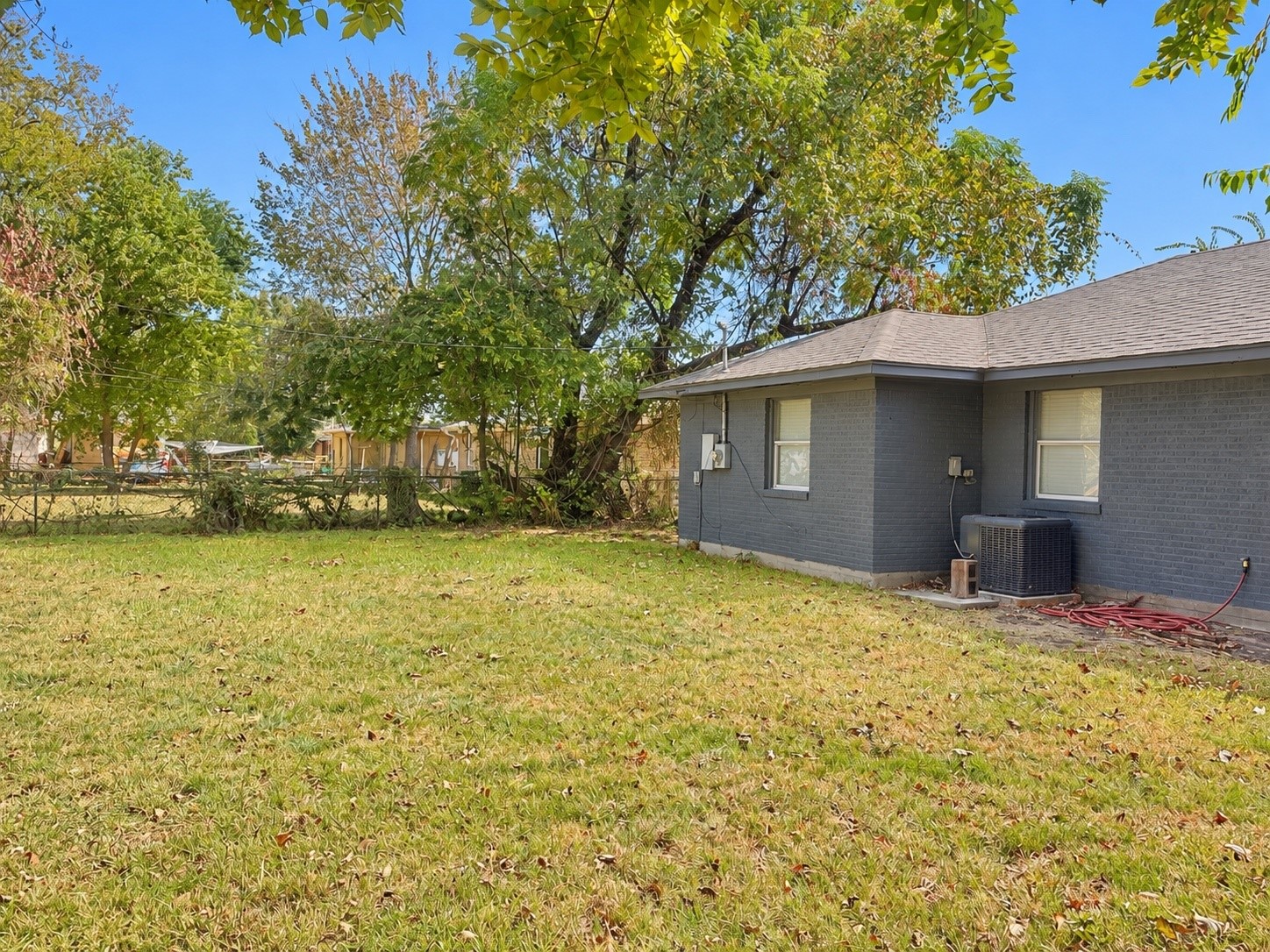 Spacious backyard with lush greenery and a charming gray brick exterior, perfect for outdoor activities and relaxation.