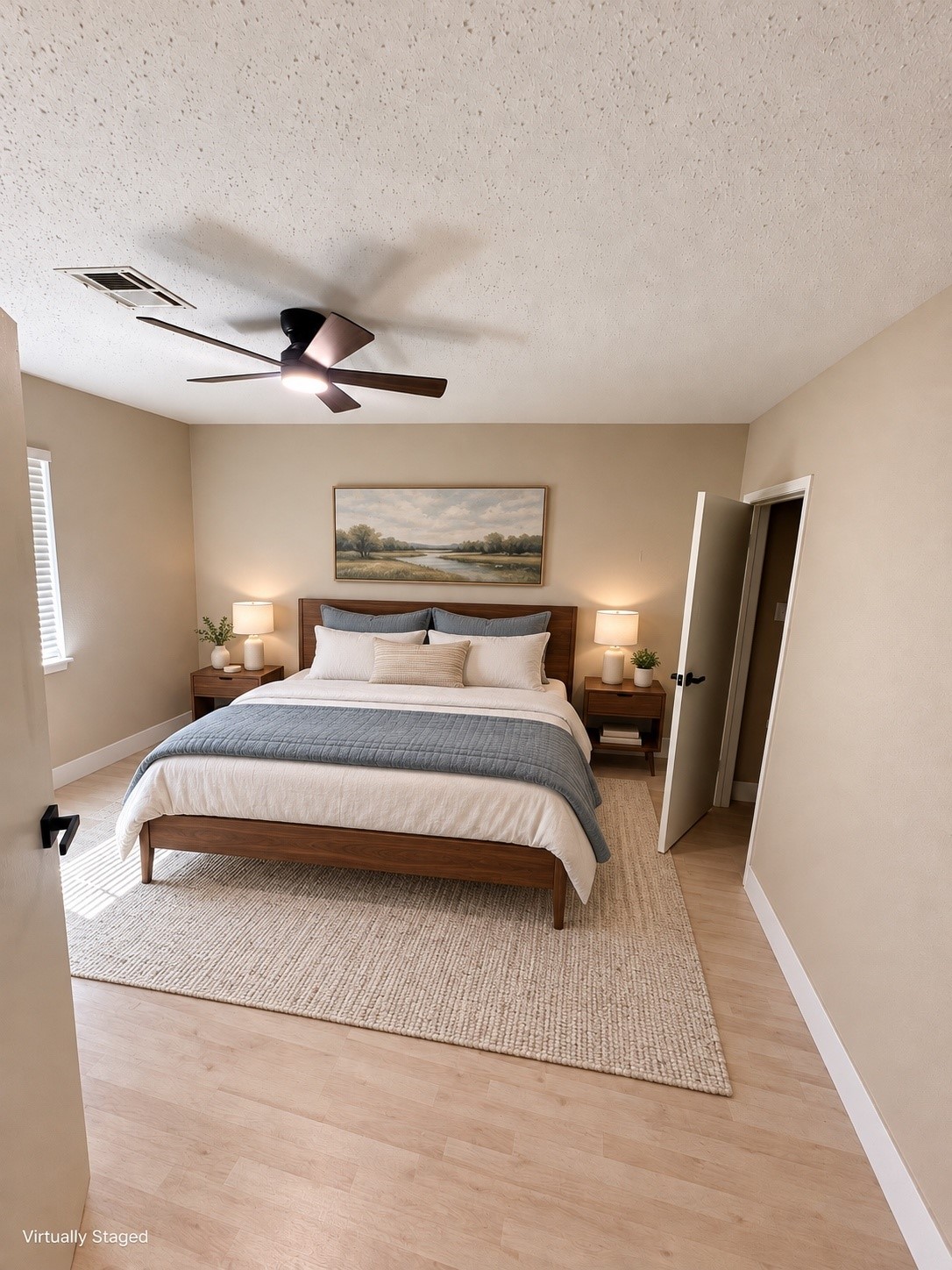 A cozy bedroom features a plush bed with elegant bedding, complemented by bedside tables with stylish lamps, all set against soft beige walls and a light wood floor.