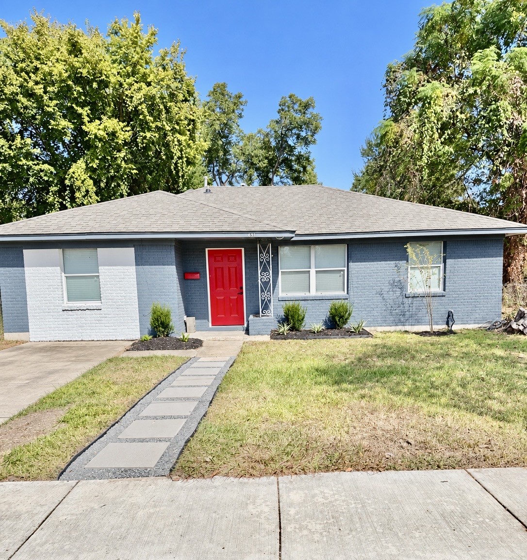 Charming single-story home with a bold red front door and modern gray exterior, surrounded by lush greenery and a neatly landscaped front yard. Charming single-story home with a bold red front door and modern gray exterior, surrounded by lush greenery and a neatly landscaped front yard.