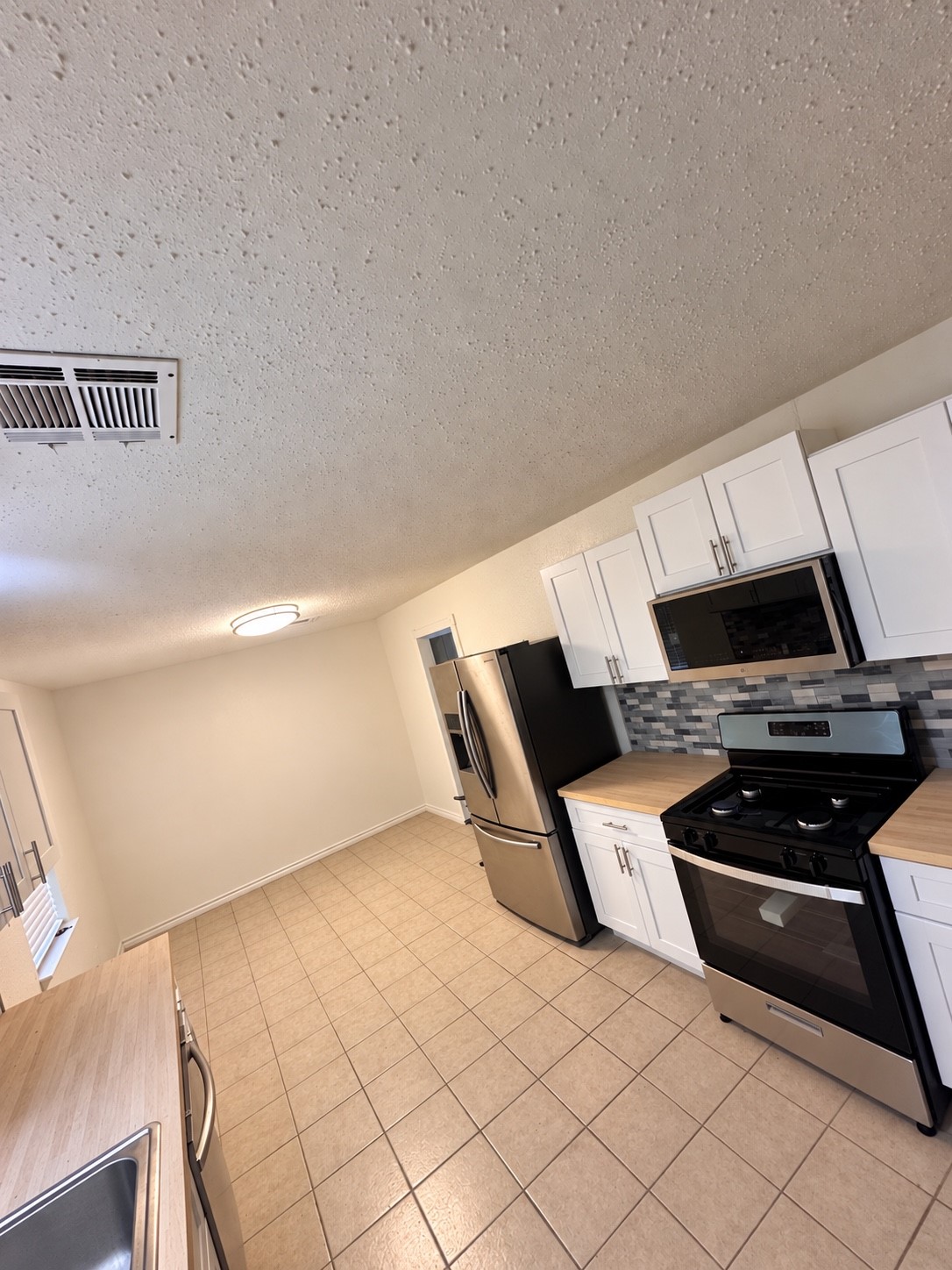 Spacious kitchen featuring modern stainless steel appliances, sleek white cabinetry, and a stylish tile backsplash, complemented by ample counter space and tiled flooring.
