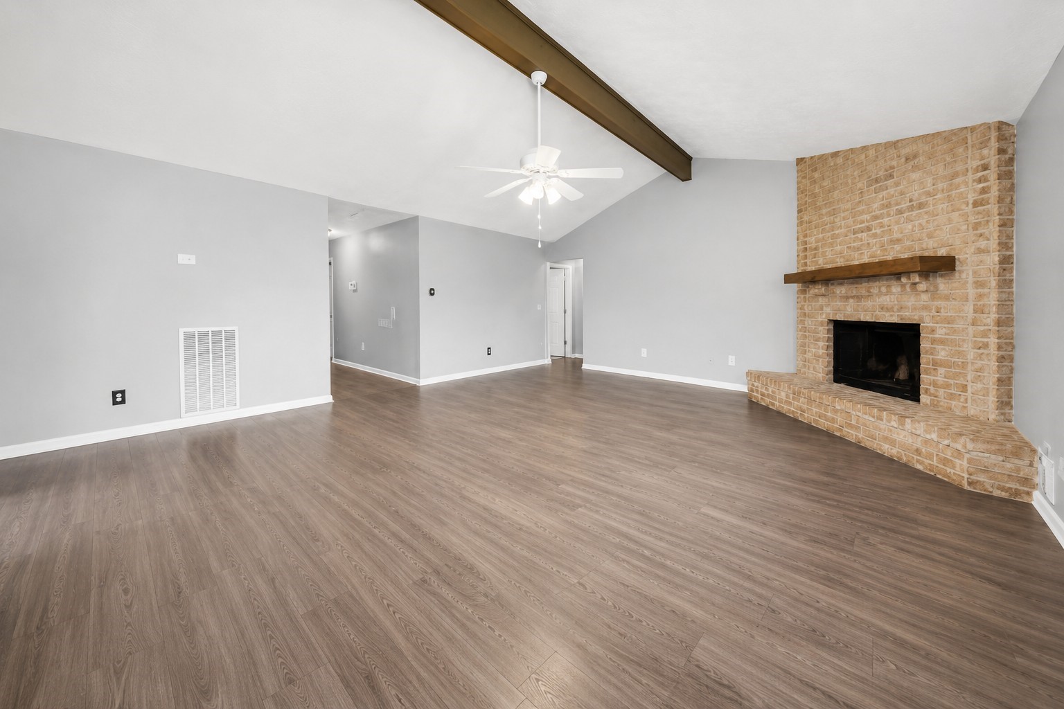 Another view of the spacious living area showcasing the brick fireplace and vaulted ceiling with exposed wood beam. Another view of the spacious living area showcasing the brick fireplace and vaulted ceiling with exposed wood beam.
