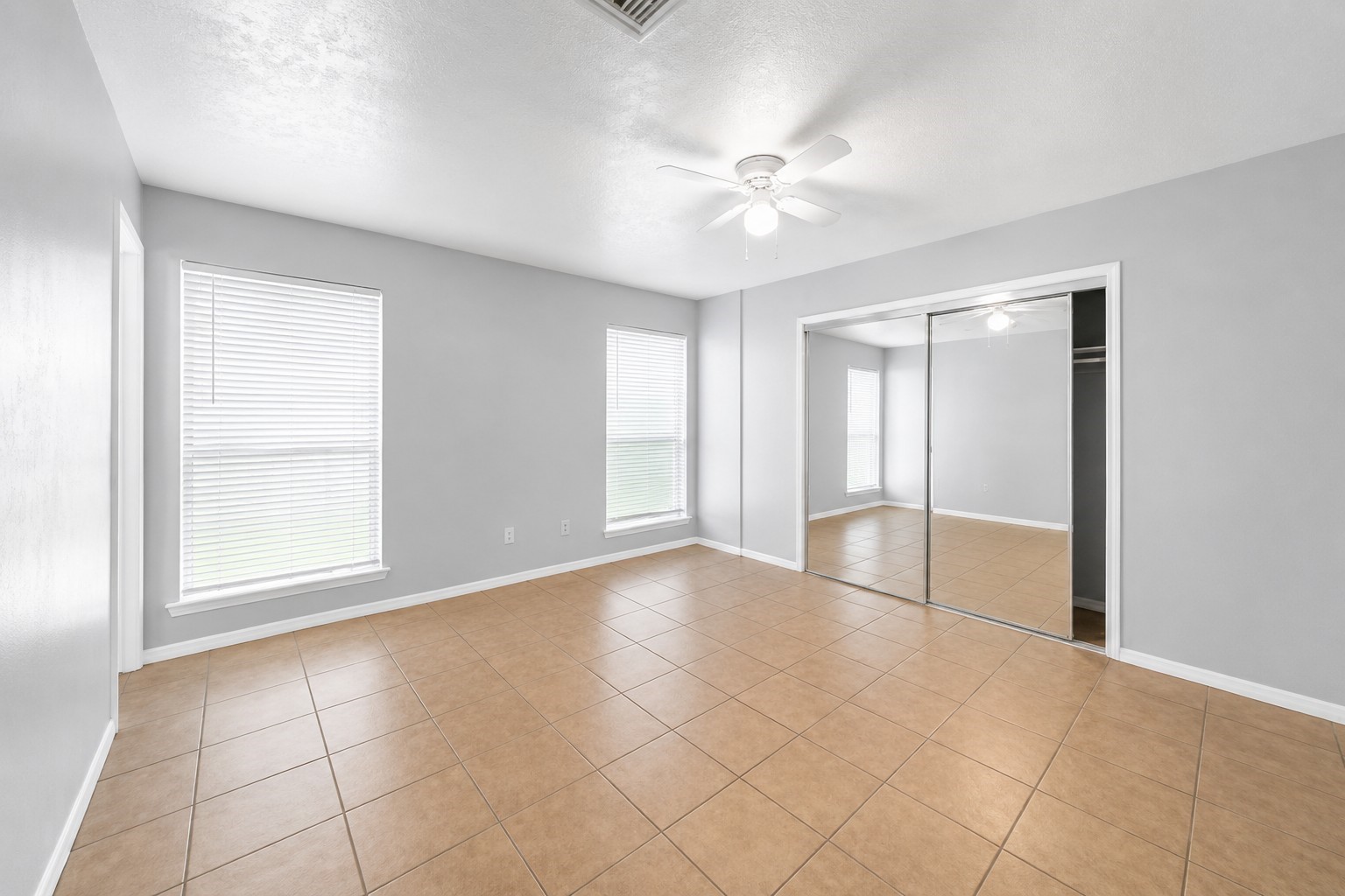 Spacious primary bedroom featuring tile flooring, abundant natural light, and a large mirrored closet.