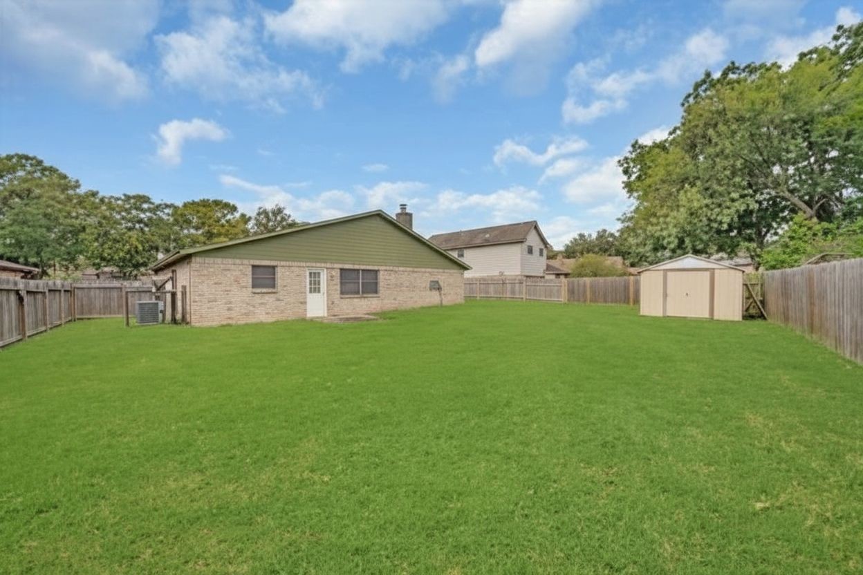 Another view of the oversized fenced backyard featuring plenty of open lawn space and a storage shed.