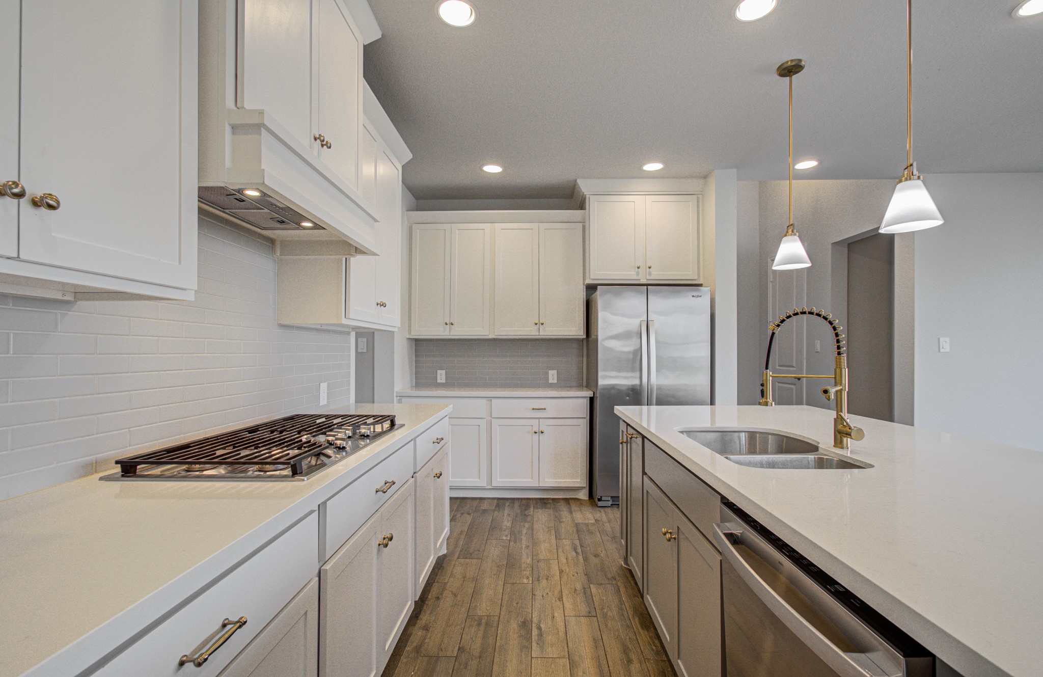 Elegant kitchen featuring sleek stainless steel appliances, a spacious island with dual sinks, modern pendant lighting, and stylish white cabinetry set against a chic subway tile backsplash.