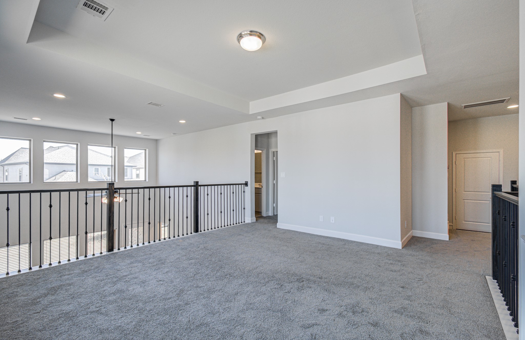 Plush carpeting, modern railing, and ample natural light from large windows, offering a versatile space for relaxation or entertainment.