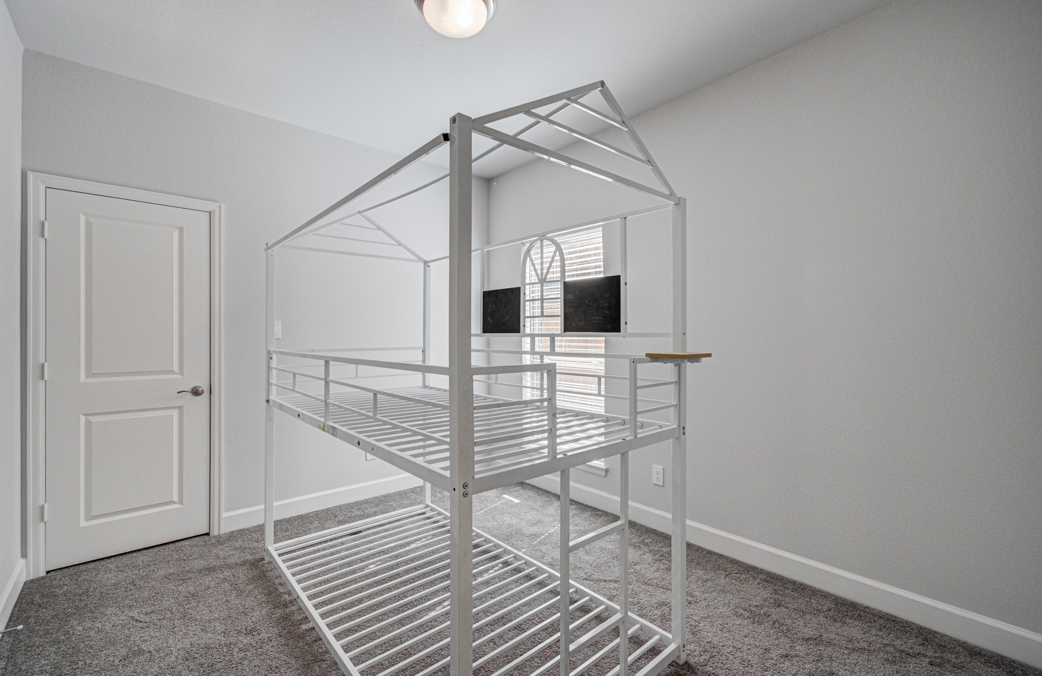 A cozy secondary bedroom located on the first floor features soft carpeting and ample natural light from a large window.