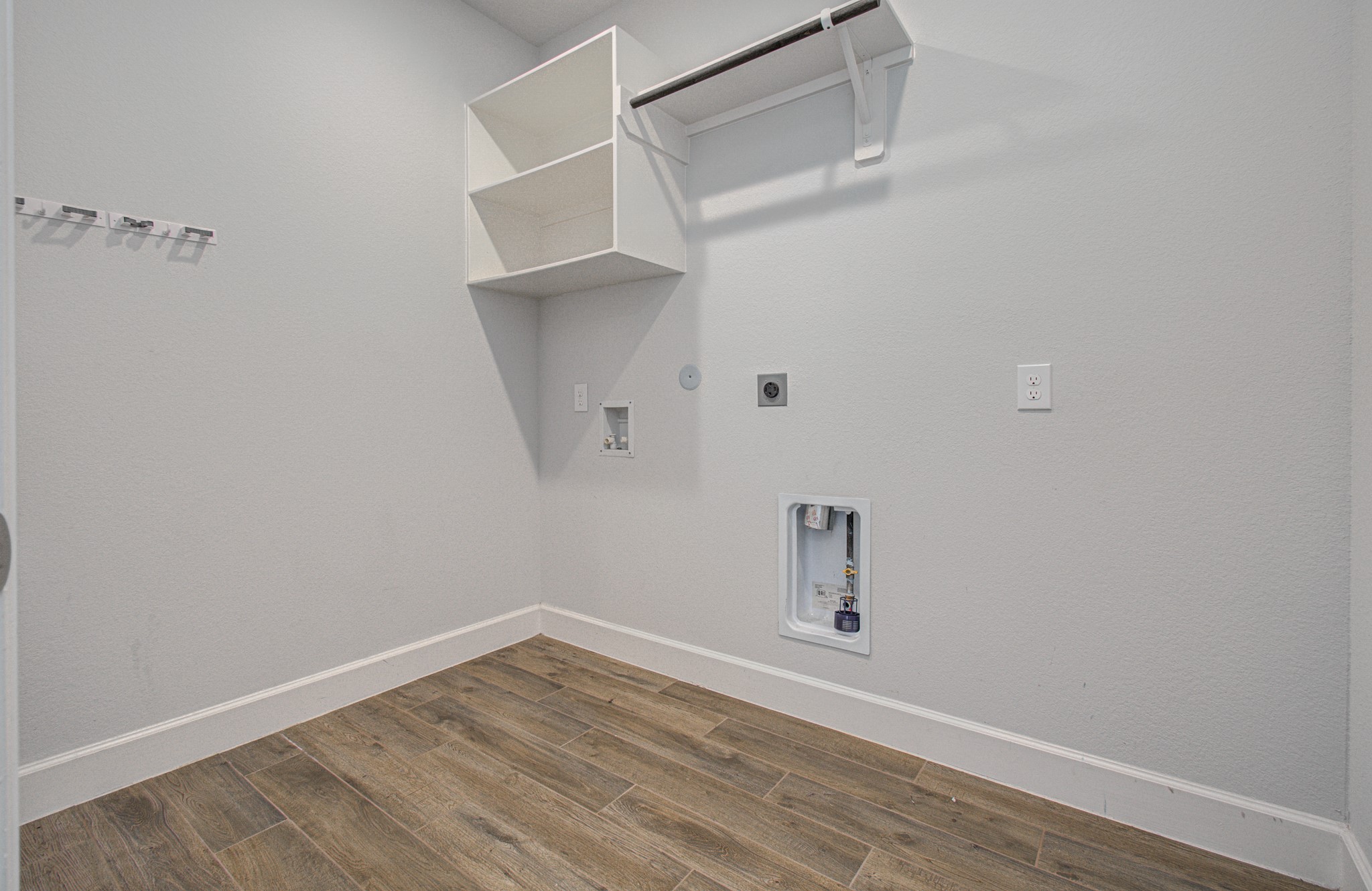 Spacious laundry room with sleek flooring, built-in shelving, and ample space for washer and dryer setup.