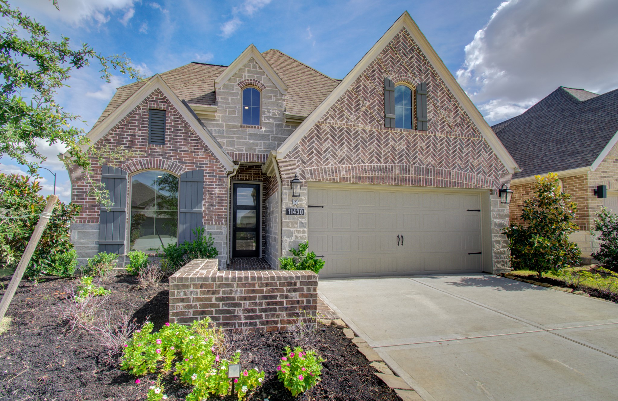 Charming brick home featuring a gabled roof, elegant arched windows with shutters, and a spacious two-car garage. Lush landscaping enhances curb appeal.