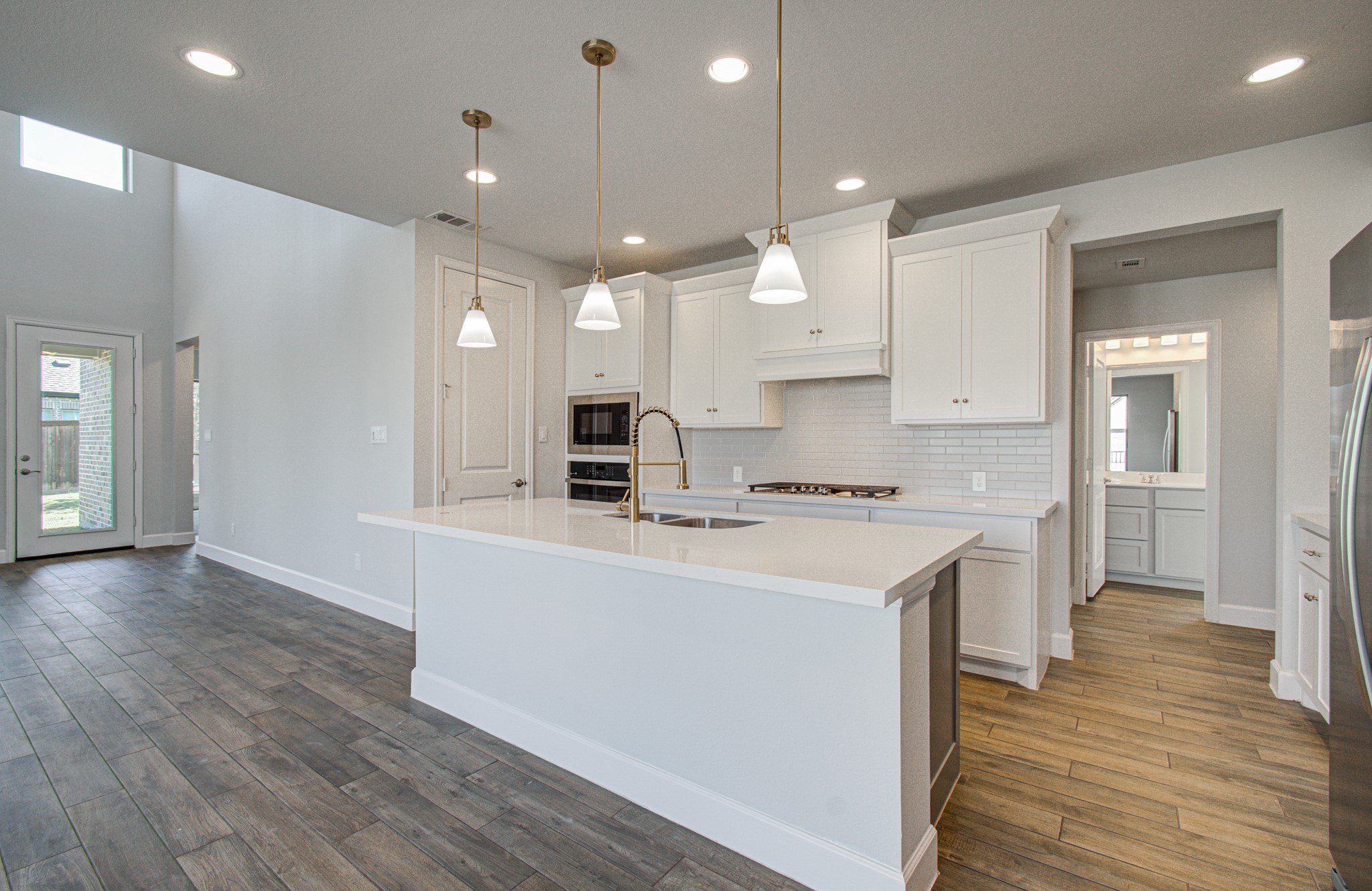 Bright and spacious kitchen featuring modern white cabinetry, a large island with pendant lighting, and sleek stainless steel appliances, seamlessly flowing into an open living area with wood-look flooring.