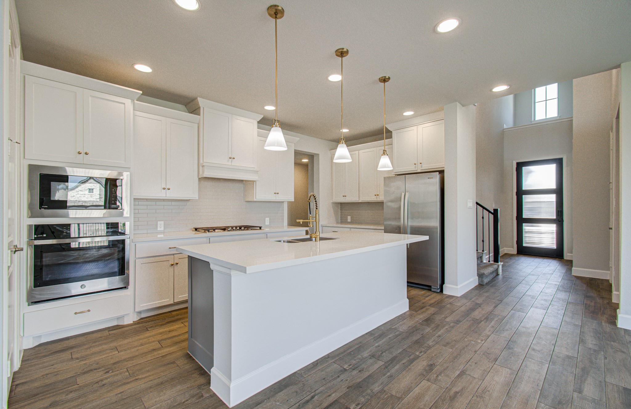A modern kitchen featuring sleek white cabinetry, stainless steel appliances, and a spacious island with pendant lighting, complemented by elegant wood-look flooring and an open, airy layout. A modern kitchen featuring sleek white cabinetry, stainless steel appliances, and a spacious island with pendant lighting, complemented by elegant wood-look flooring and an open, airy layout.