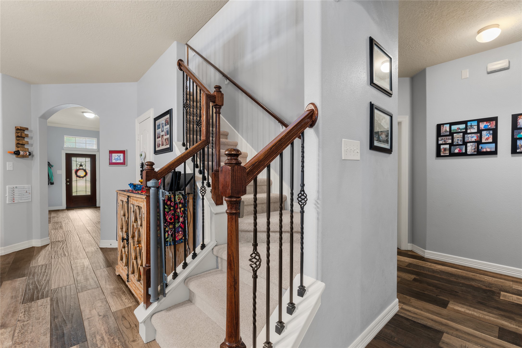Inviting entryway with elegant wood and wrought iron staircase, complemented by warm wood flooring and soft gray walls.