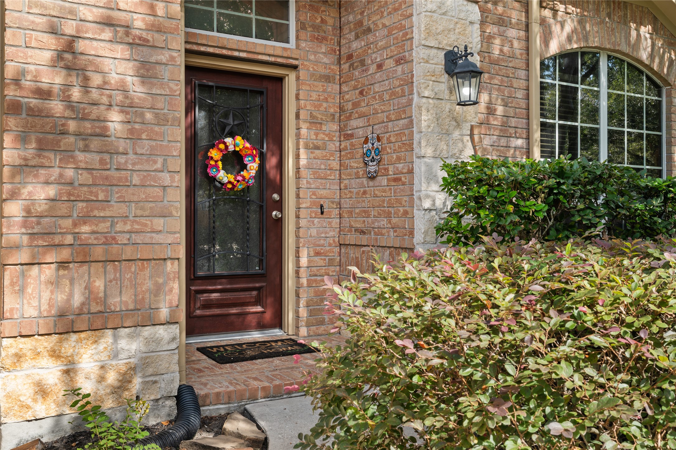 Charming brick entryway features a welcoming door adorned with a colorful wreath, complemented by a decorative lantern and lush greenery. Charming brick entryway features a welcoming door adorned with a colorful wreath, complemented by a decorative lantern and lush greenery.