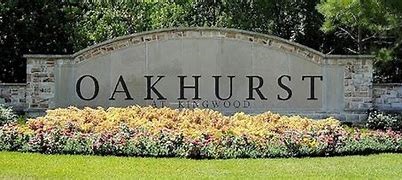 Welcome to Oakhurst at Kingwood, a beautifully landscaped community entrance surrounded by lush greenery and vibrant flowers.