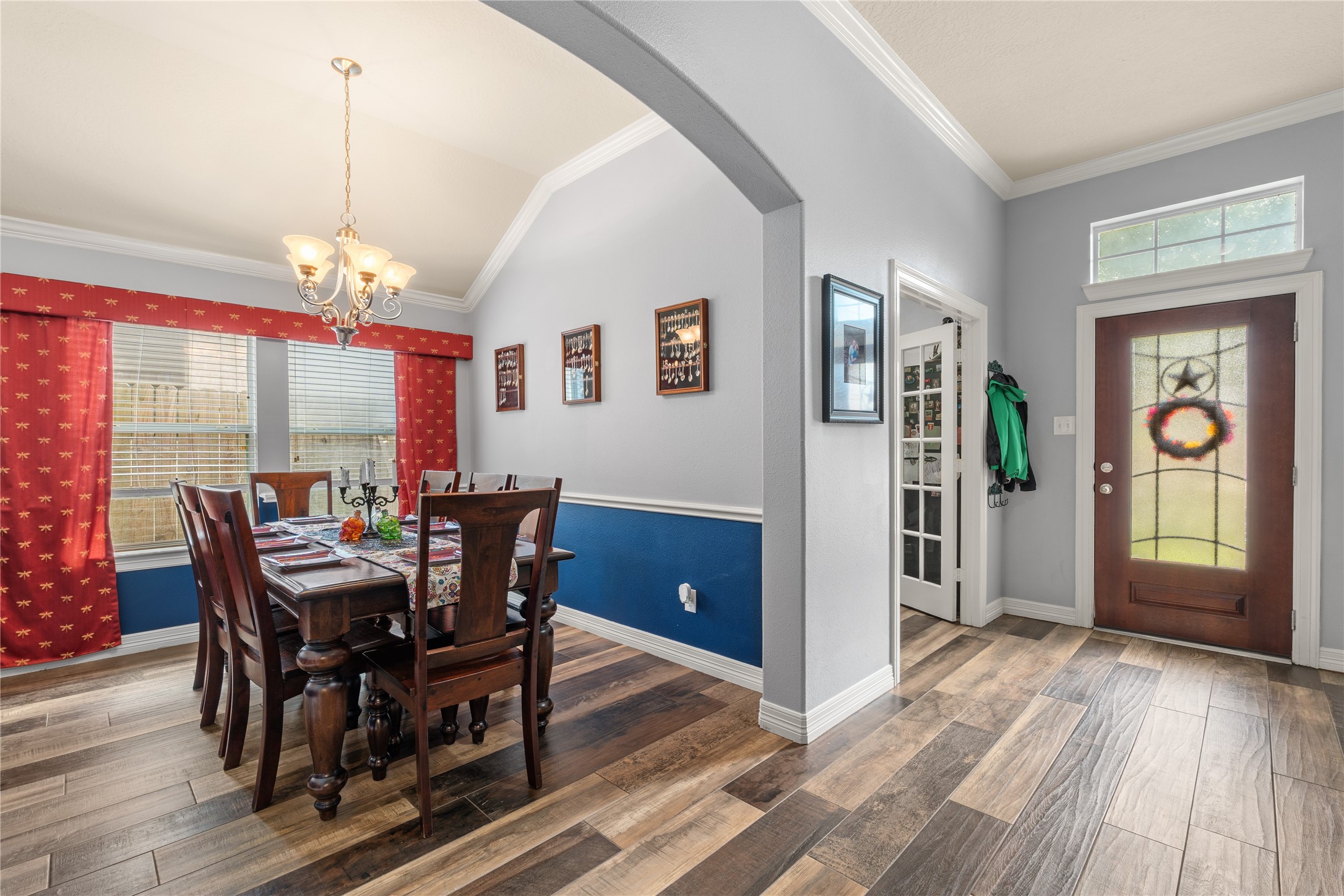 Inviting dining area with elegant chandelier, rich wood flooring, and vibrant red curtains, seamlessly connected to a welcoming entryway with a decorative glass front door. Inviting dining area with elegant chandelier, rich wood flooring, and vibrant red curtains, seamlessly connected to a welcoming entryway with a decorative glass front door.