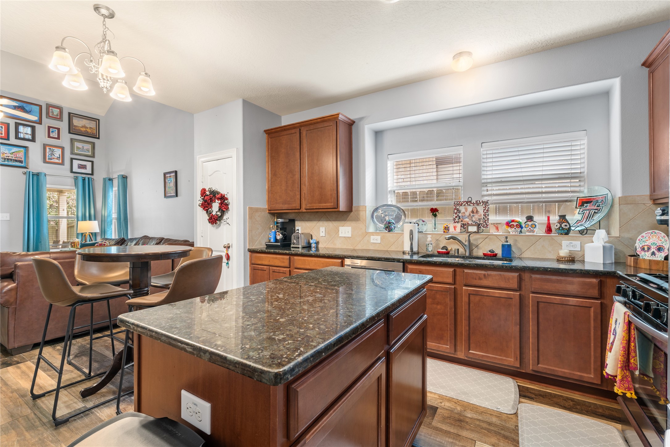 Spacious kitchen with rich wooden cabinetry and granite countertops, featuring a central island and a cozy dining nook with stylish bar seating. Natural light pours in through large windows, creating a warm and inviting atmosphere.