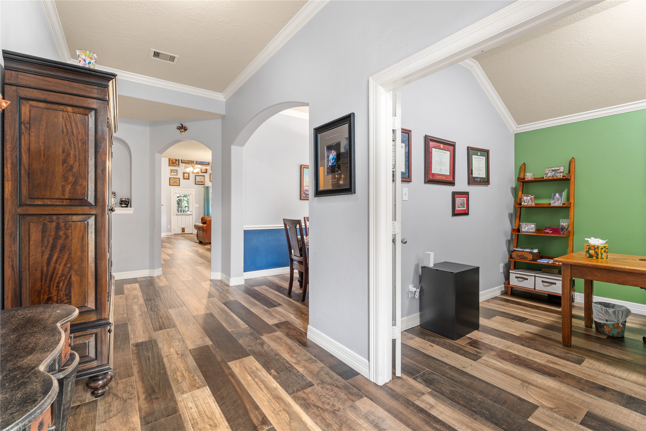 Charming interior featuring elegant wood flooring, archways leading to a cozy living area, and a bright office space with vibrant green accents.