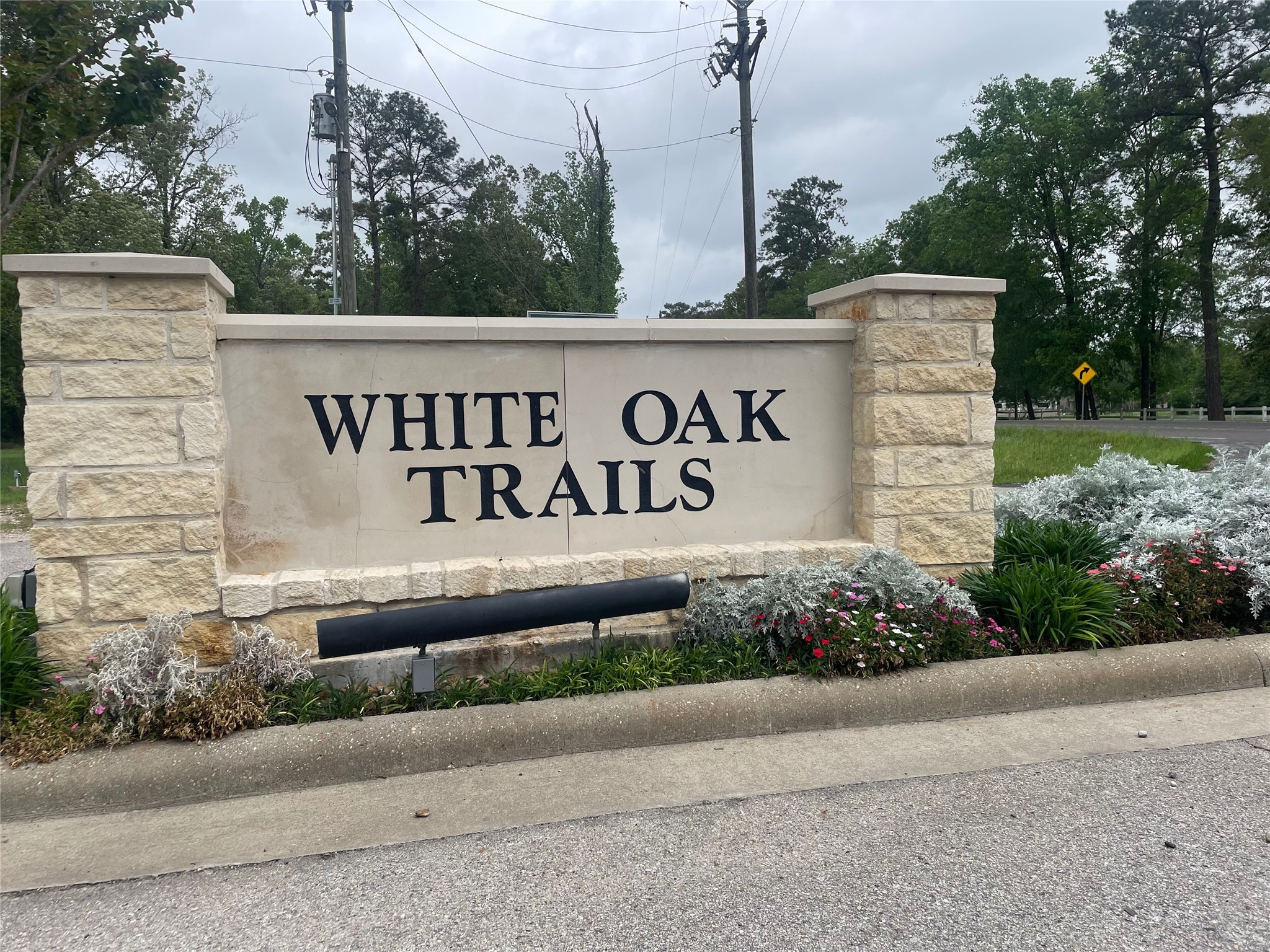 The photo shows the entrance to "White Oak Trails," featuring a stone sign with neatly landscaped surroundings and mature trees, creating a welcoming and natural ambiance for potential home buyers.