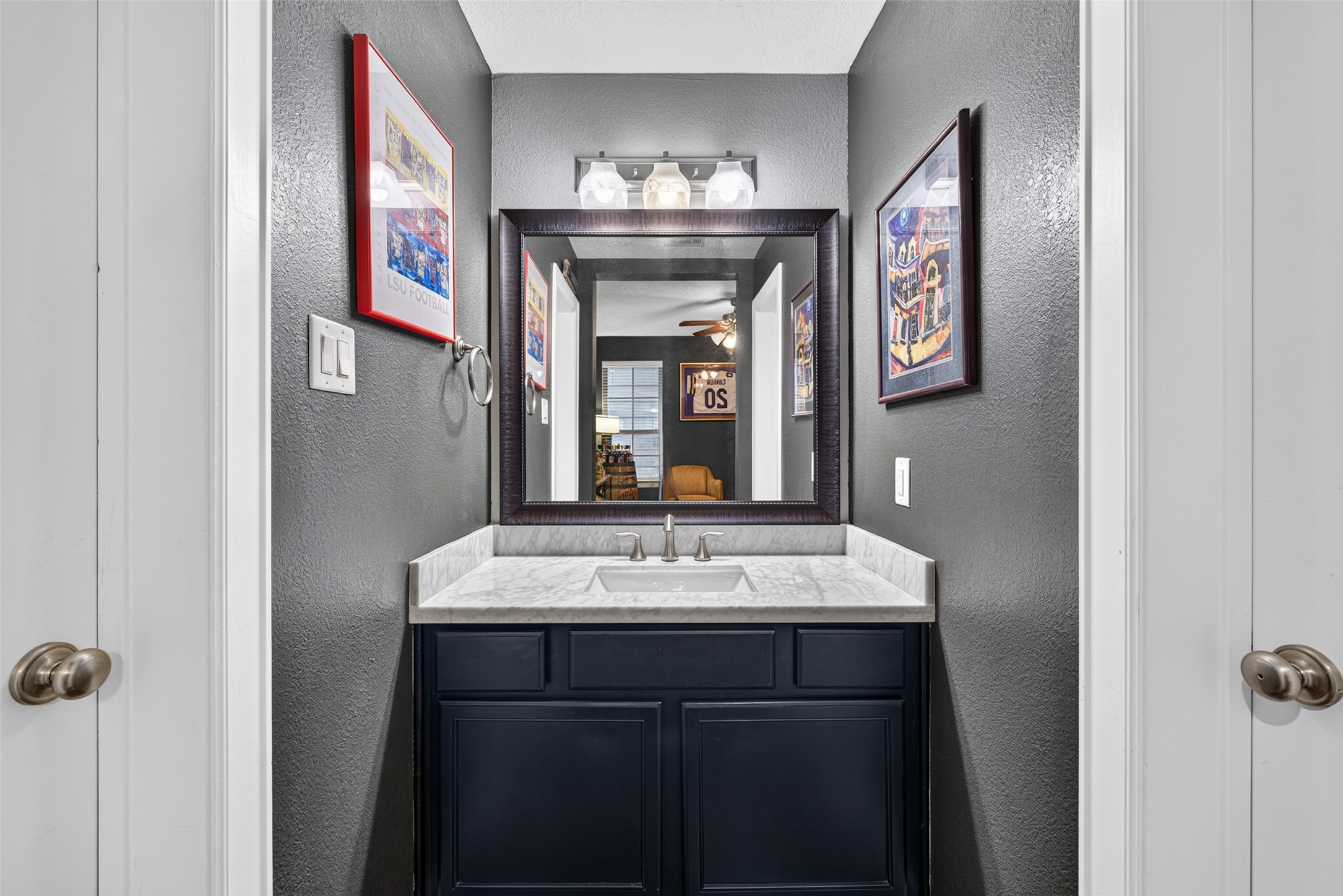 Attached full bath serving the flexible downstairs guest bedroom or home office, featuring a dark vanity and framed mirror.