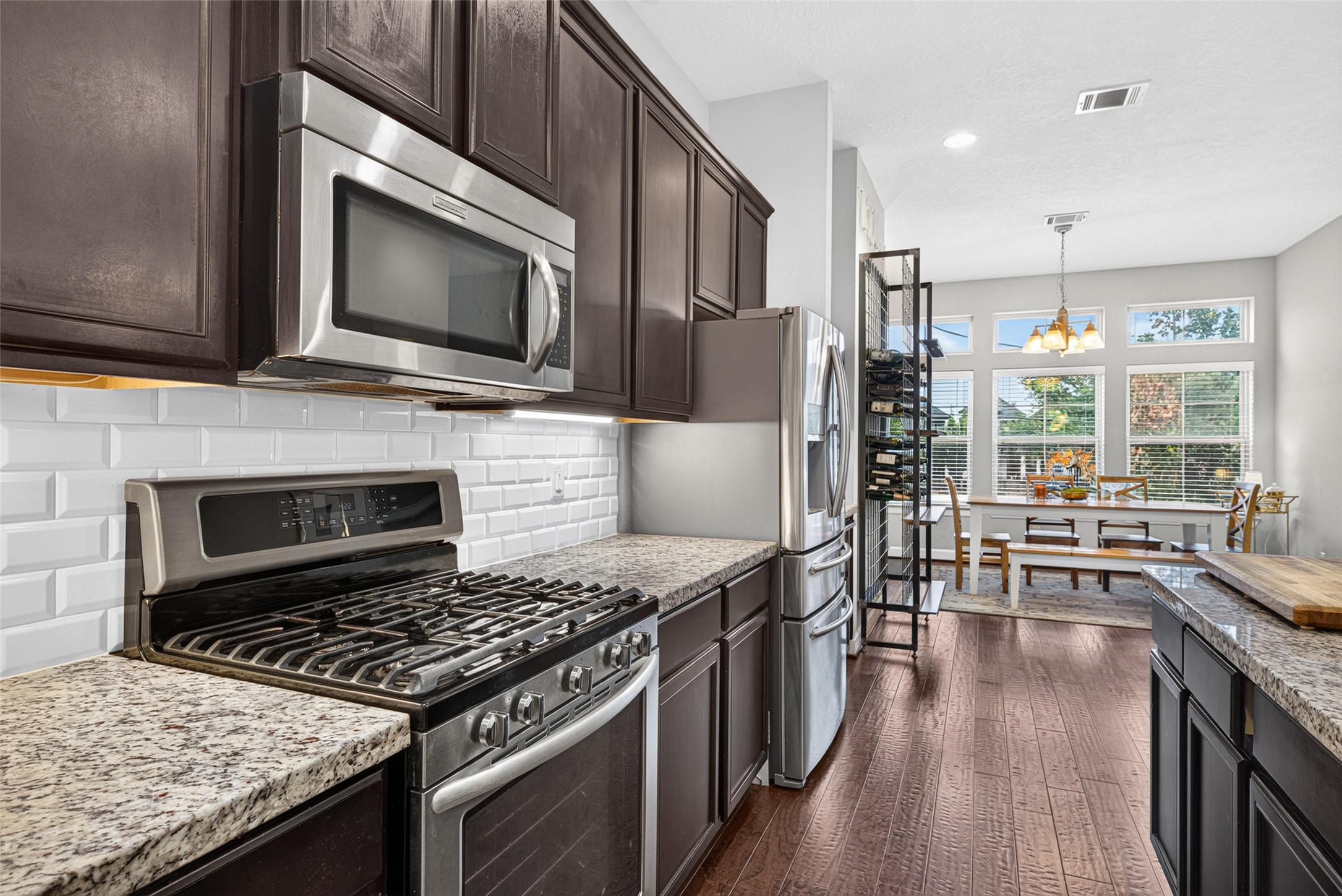 Stainless steel gas range, built-in microwave, and subway tile backsplash complement the kitchen's warm finishes.