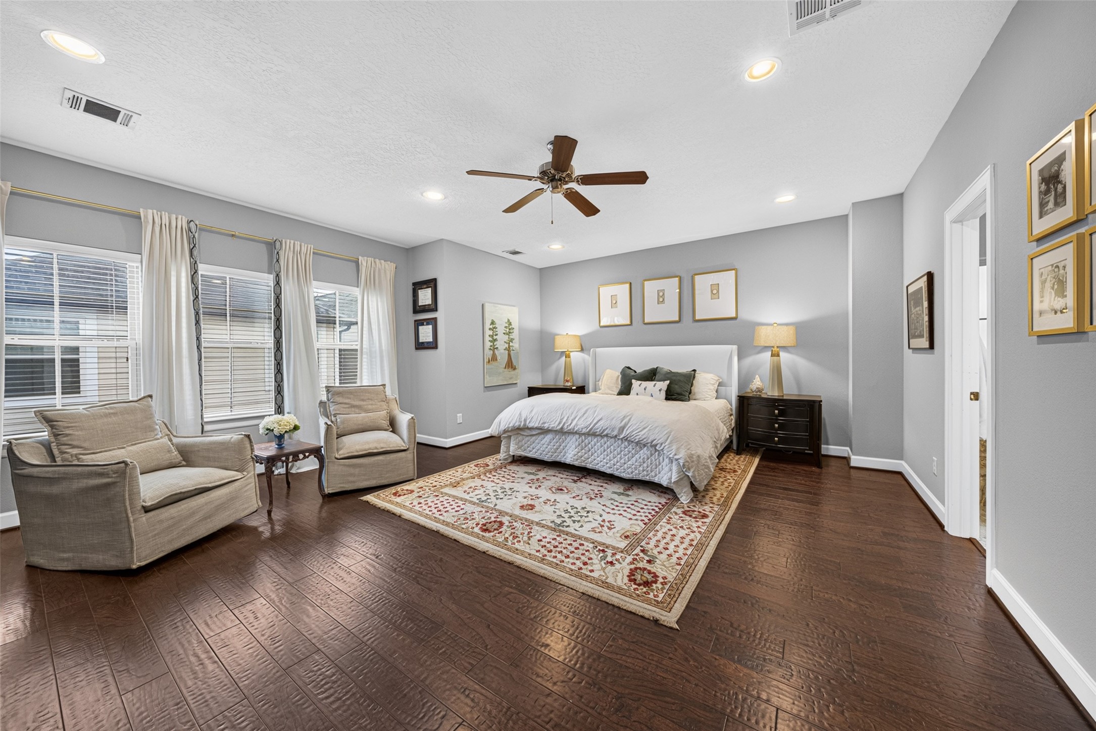 Spacious primary bedroom with hardwood floors, recessed lighting, and a comfortable sitting area.