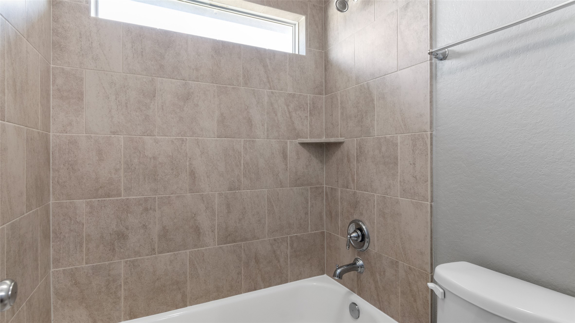 Bath/Shower combo, with a window up high bringing in a lot of natural lighting.