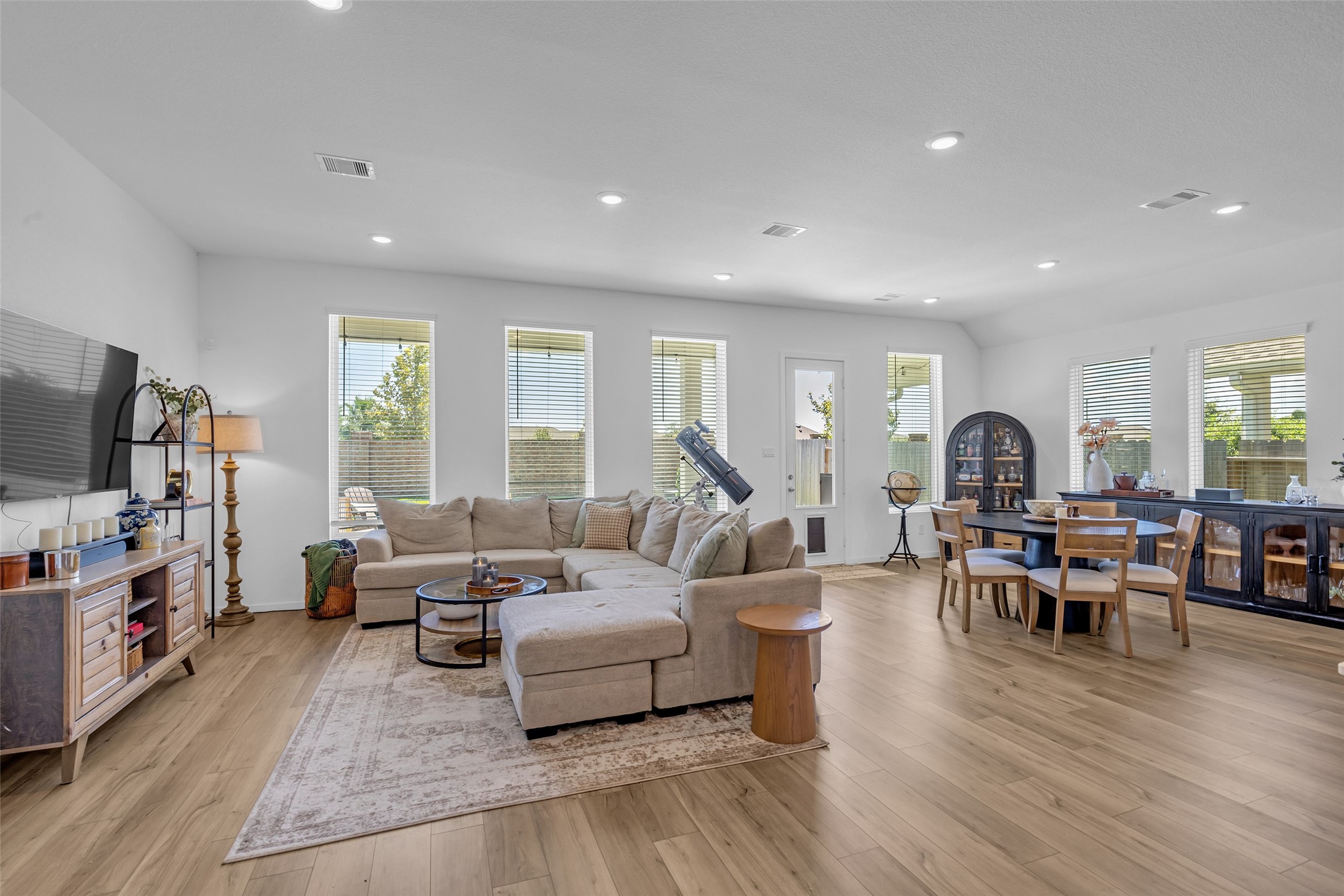 Spacious and bright open-concept living area featuring hardwood floors, large windows, and a cozy sectional sofa, seamlessly connected to a dining space with modern furnishings.
