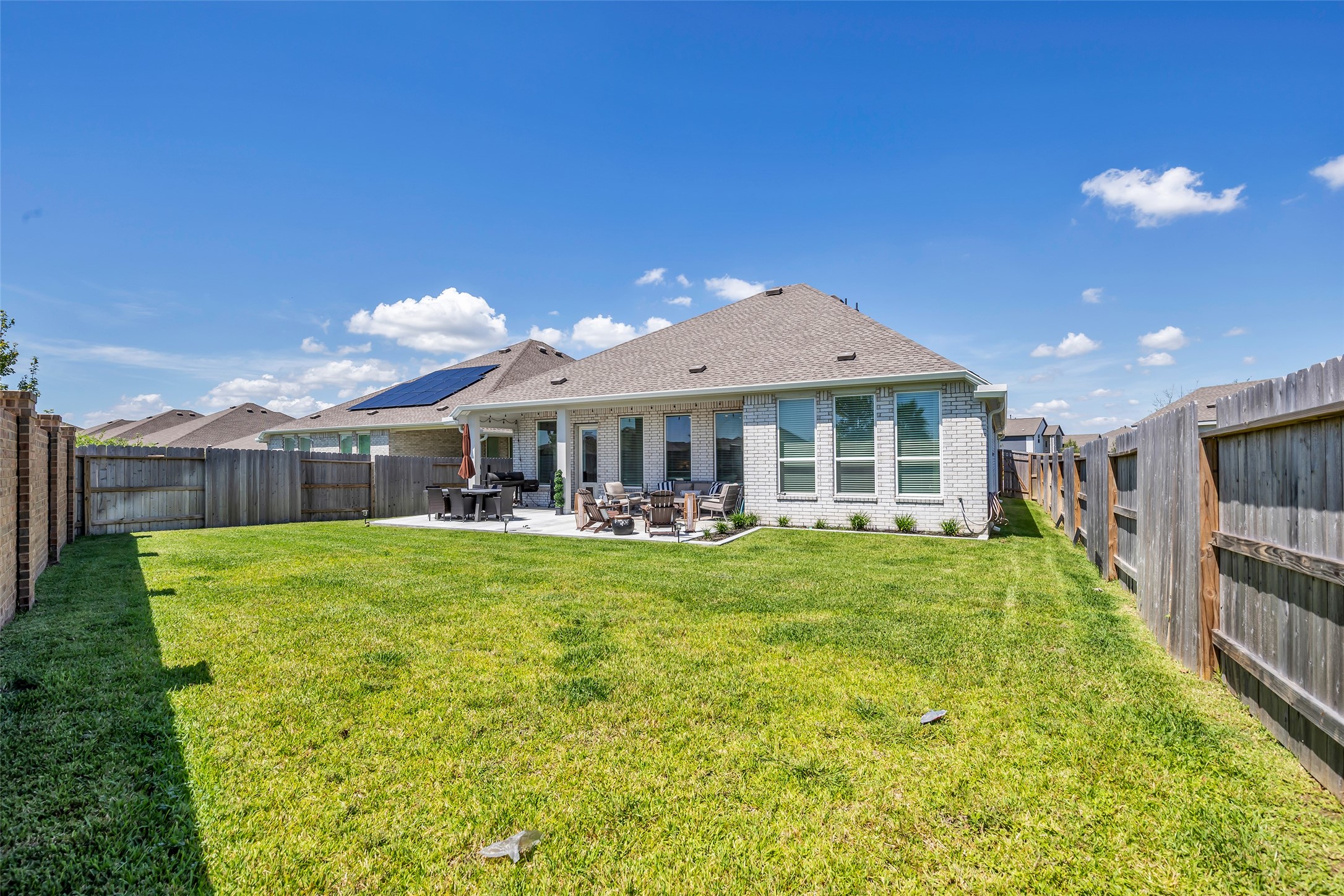 Expansive backyard with lush green lawn, perfect for outdoor gatherings, featuring a cozy patio area ideal for dining and relaxation.