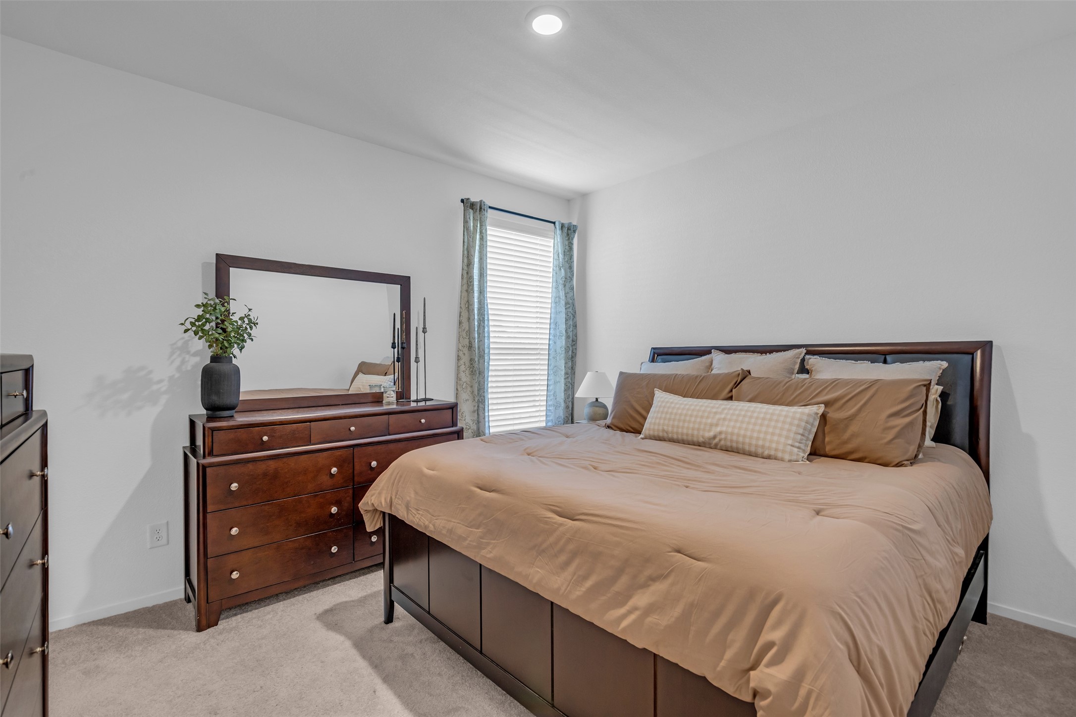 Cozy bedroom featuring a plush bed with neutral bedding, a stylish dresser with a mirror, and soft carpeting, creating a warm and inviting atmosphere.