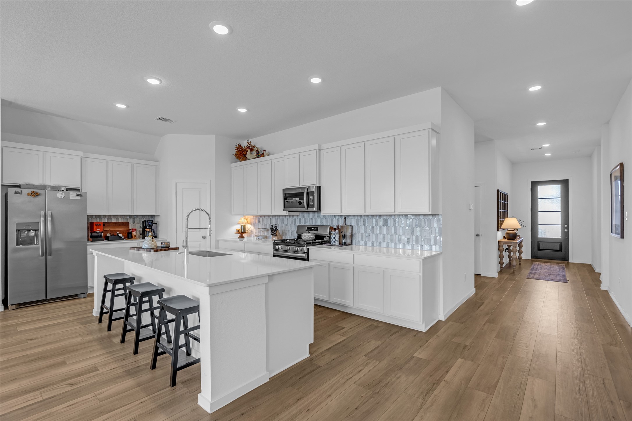 Sleek and modern kitchen with white cabinetry, stainless steel appliances, and a spacious island with seating, beautifully complemented by a stylish backsplash and warm wood flooring.