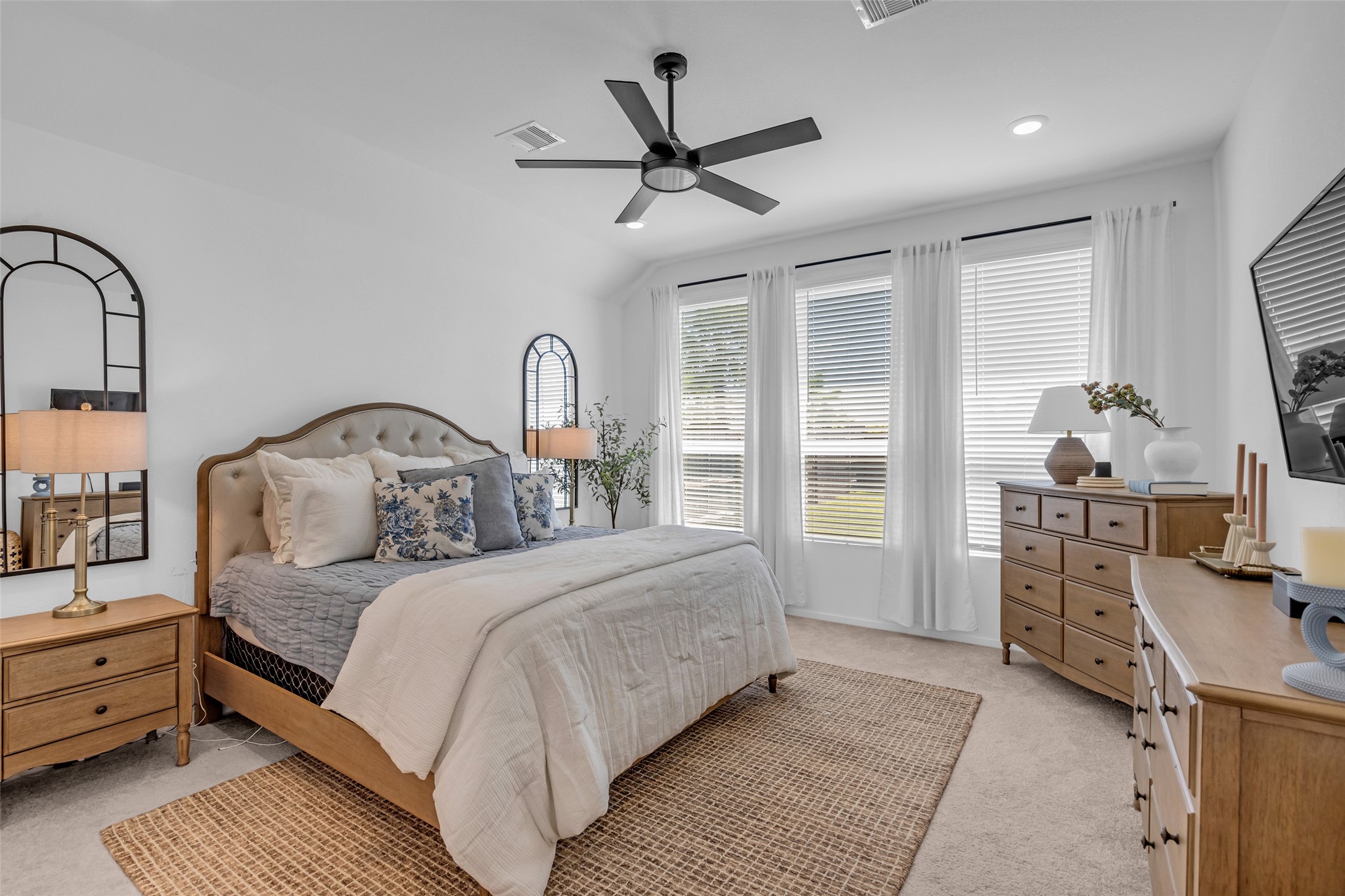 Bright and inviting bedroom featuring a cozy upholstered bed, stylish wooden furniture, and large windows that fill the space with natural light.