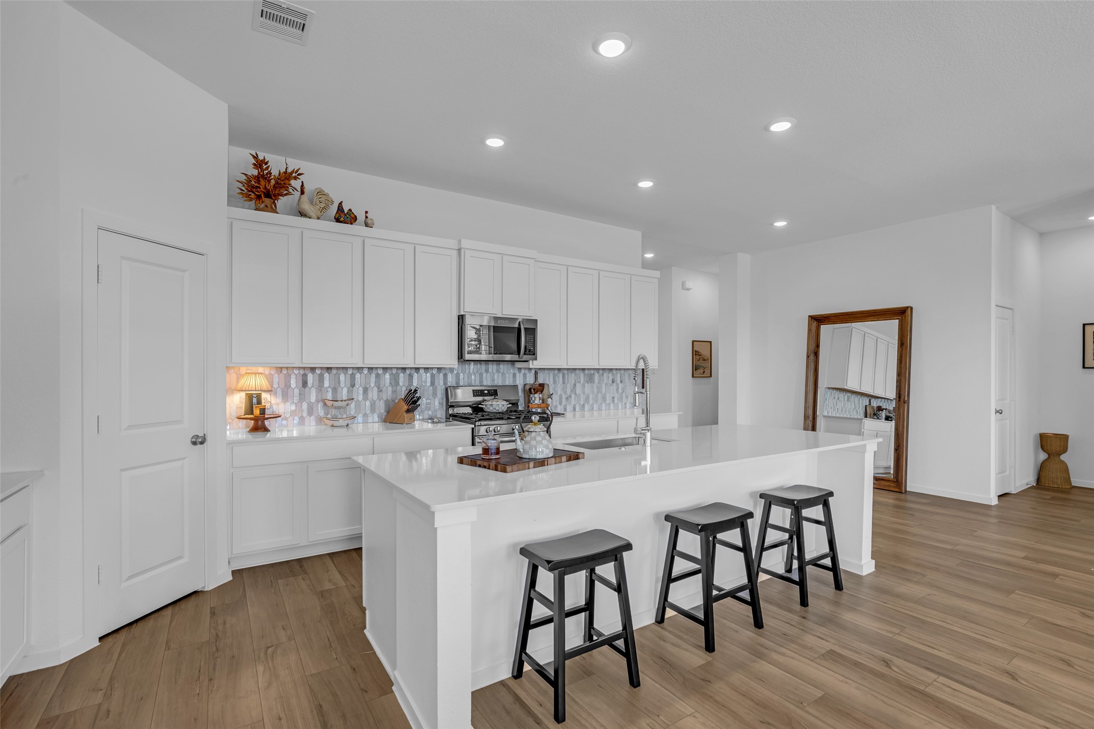 Sleek modern kitchen with white cabinetry, elegant tile backsplash, and a spacious island with seating, perfect for cooking and entertaining.