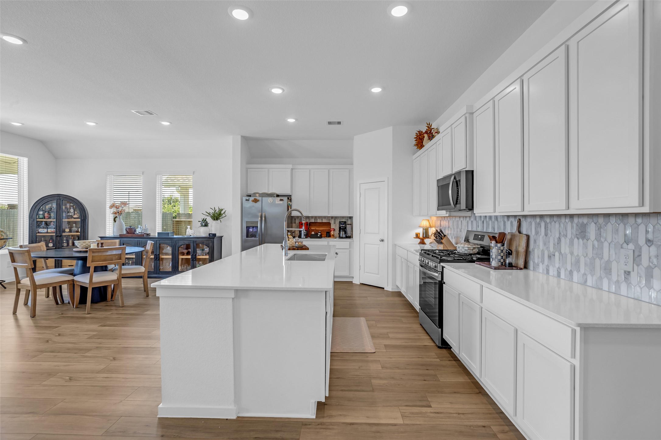 Experience modern living in this open-concept kitchen and dining area, featuring sleek white cabinetry, stainless steel appliances, and a spacious island perfect for entertaining. The adjacent dining space offers ample natural light and a cozy atmosphere.