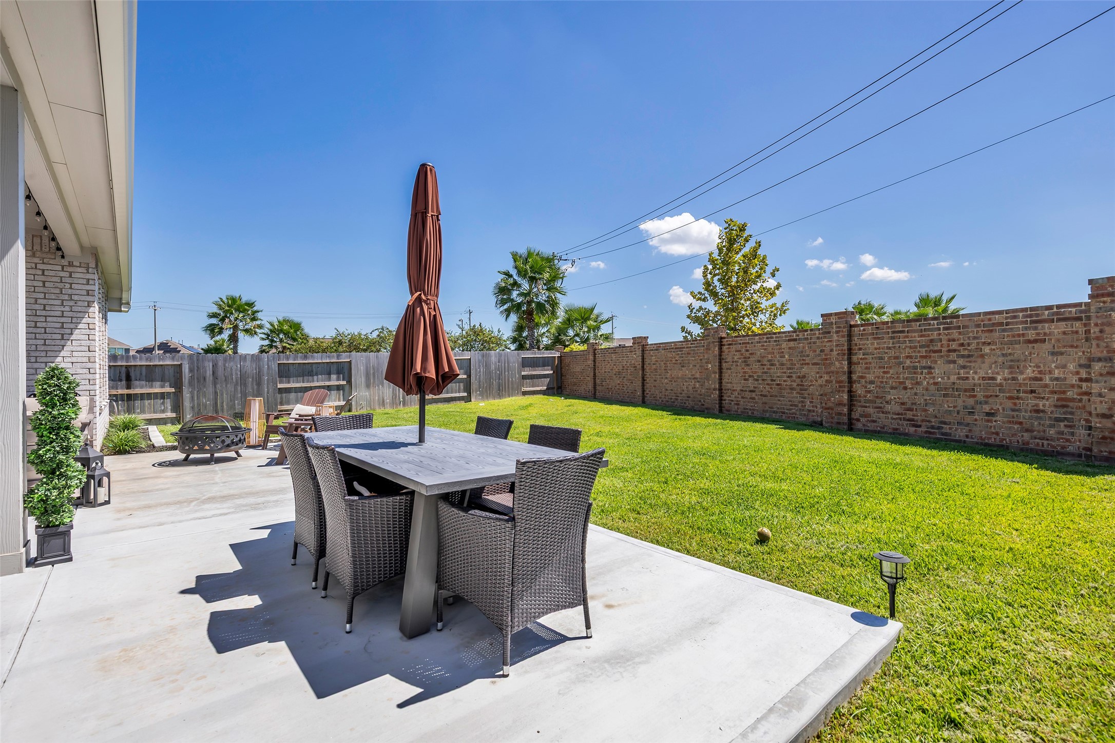 Spacious backyard patio featuring a stylish dining set, lush green lawn, and a cozy fire pit area, perfect for outdoor gatherings.
