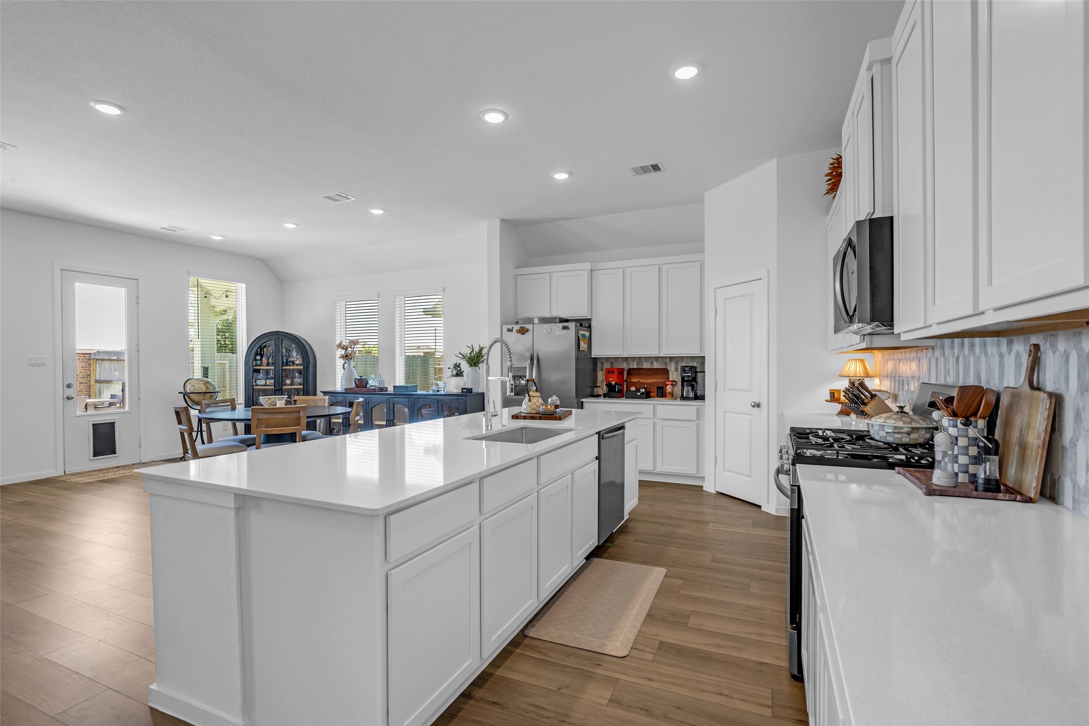 Spacious, modern kitchen with sleek white cabinetry, a large island, and stainless steel appliances, seamlessly flowing into a bright dining area.