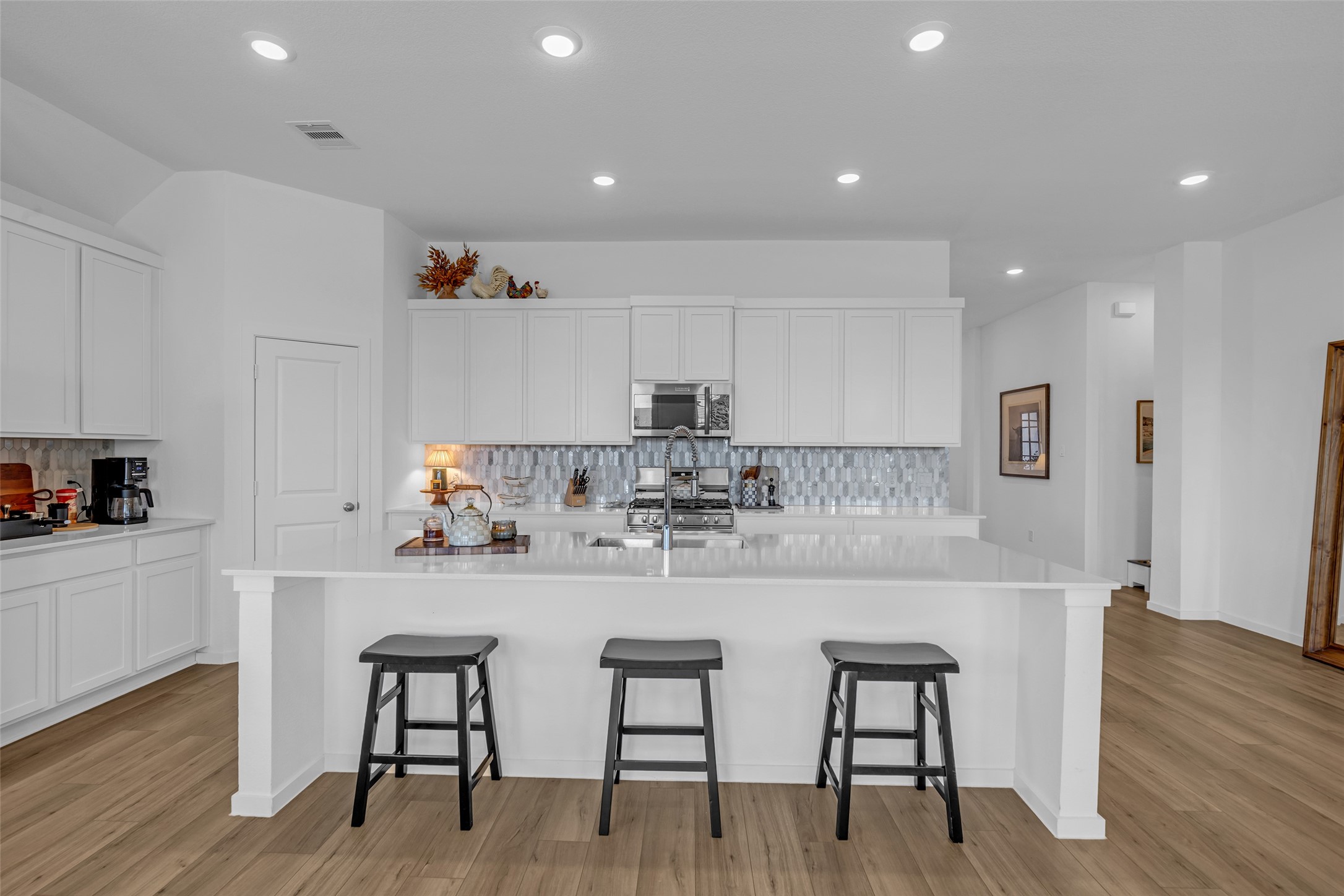 Experience the elegance of a bright, modern kitchen featuring sleek white cabinetry, a spacious island with seating, and stylish tile backsplash, all set against beautiful wood like flooring. Experience the elegance of a bright, modern kitchen featuring sleek white cabinetry, a spacious island with seating, and stylish tile backsplash, all set against beautiful wood like flooring.
