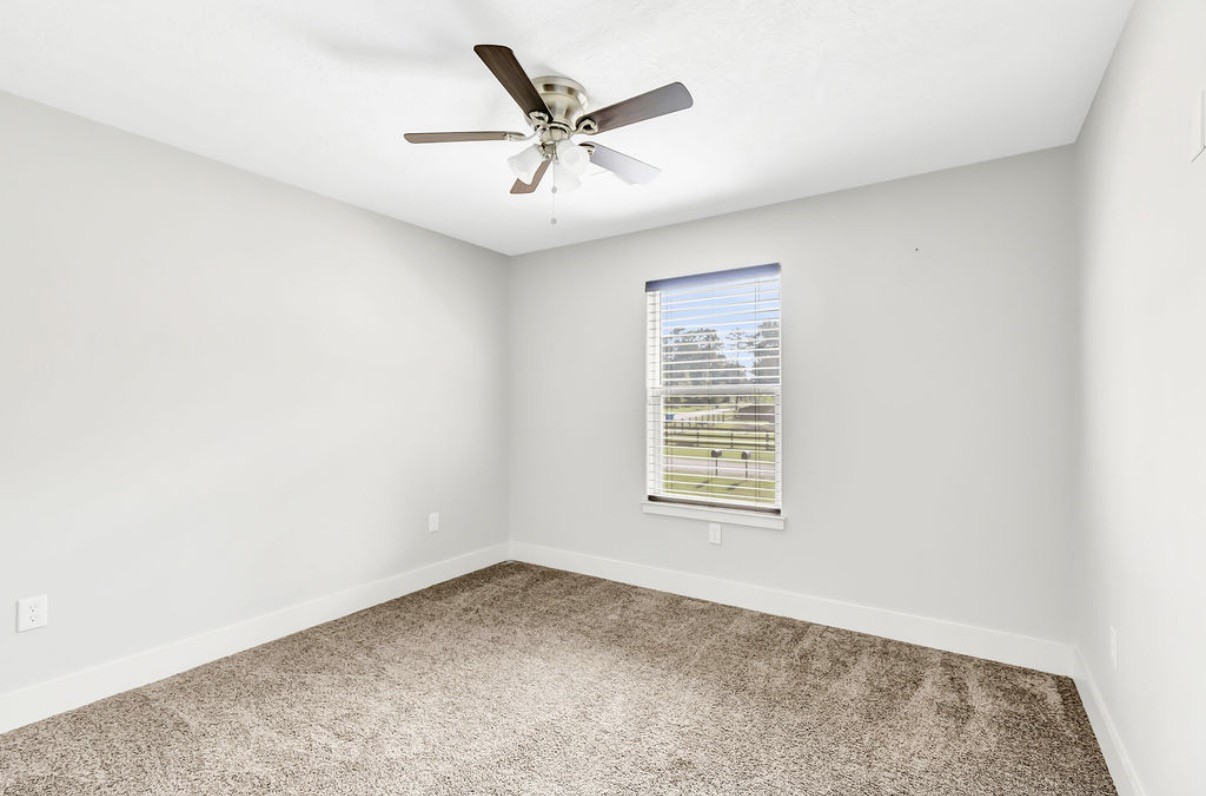 Experience serene comfort in this bright, airy bedroom with soft carpet, neutral tones, a ceiling fan, and a large window showcasing scenic views.