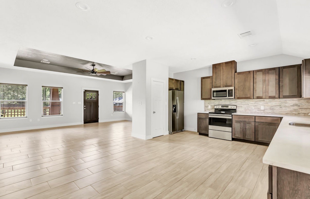 Experience the perfect blend of style and comfort in this spacious open-concept kitchen and living area, featuring modern stainless steel appliances, warm wood cabinetry, sleek tile flooring, and abundant natural light enhanced by a stylish ceiling fan.