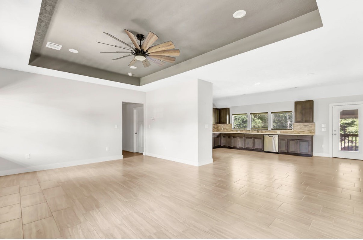 Discover the allure of a spacious open-concept living area showcasing sleek tile flooring, a modern ceiling fan, and a stylish kitchen with dark cabinetry and stainless steel appliances.