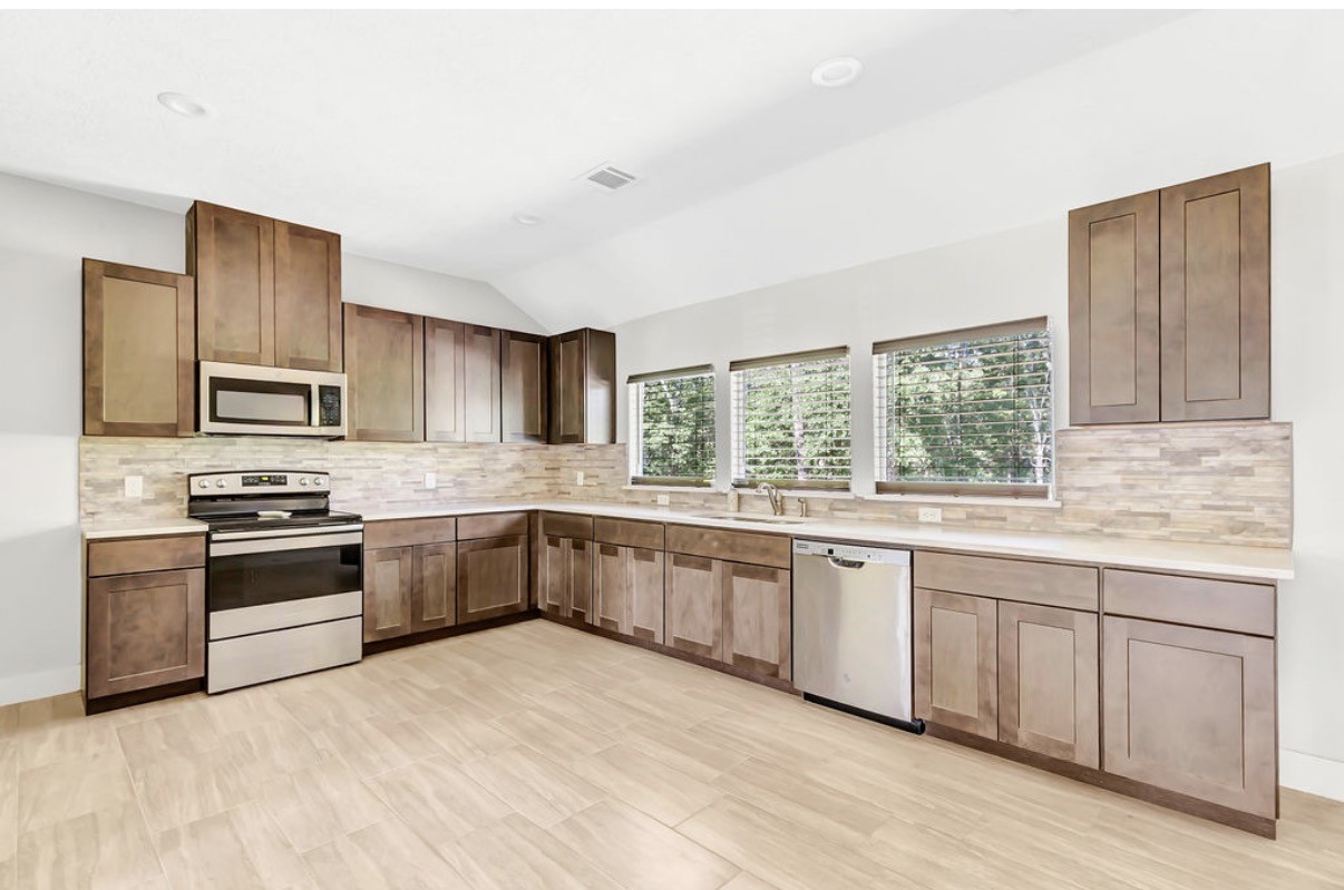 Discover a spacious kitchen featuring sleek stainless steel appliances, abundant wooden cabinetry, and large windows that flood the space with natural light.