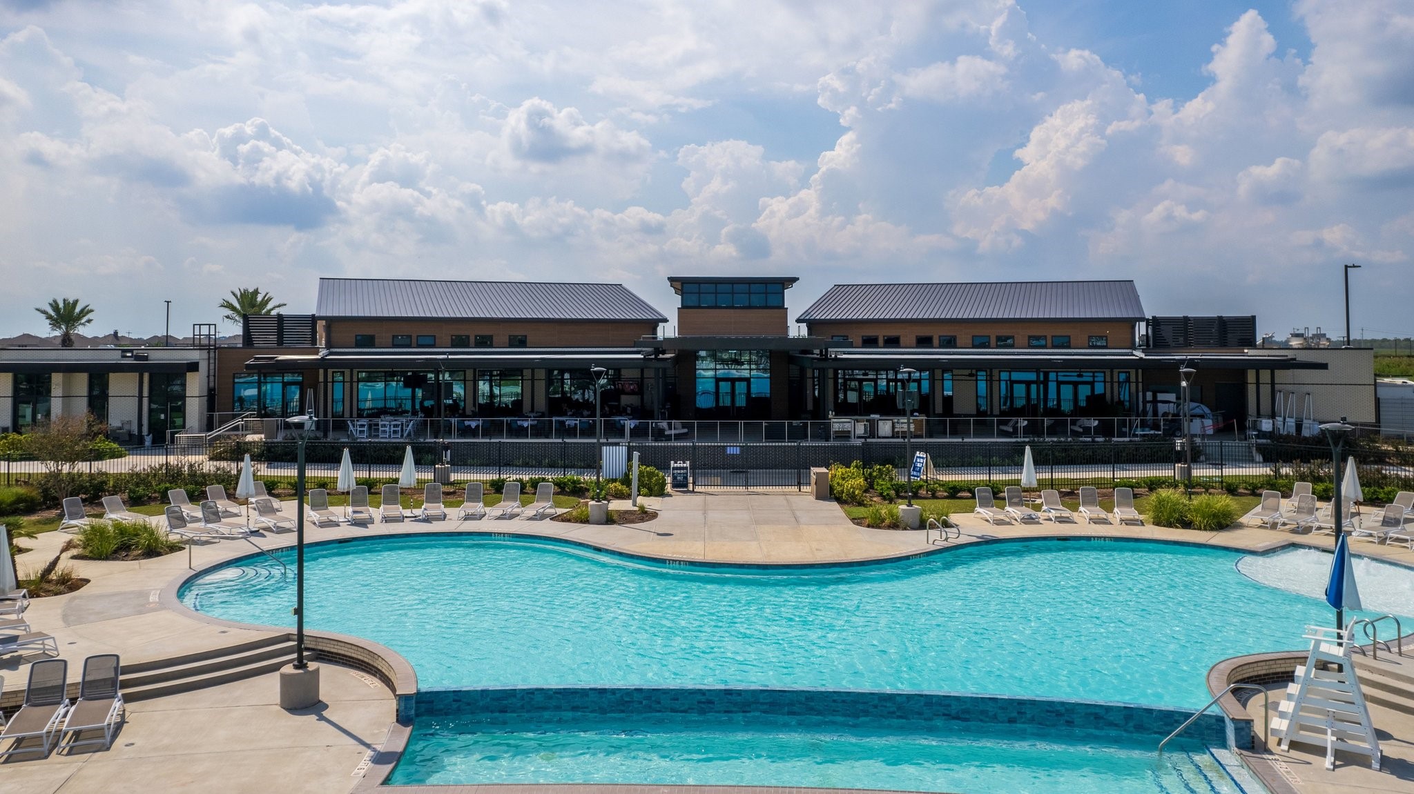 Expansive resort-style pool with abundant lounge seating and a modern clubhouse overlooking the water.