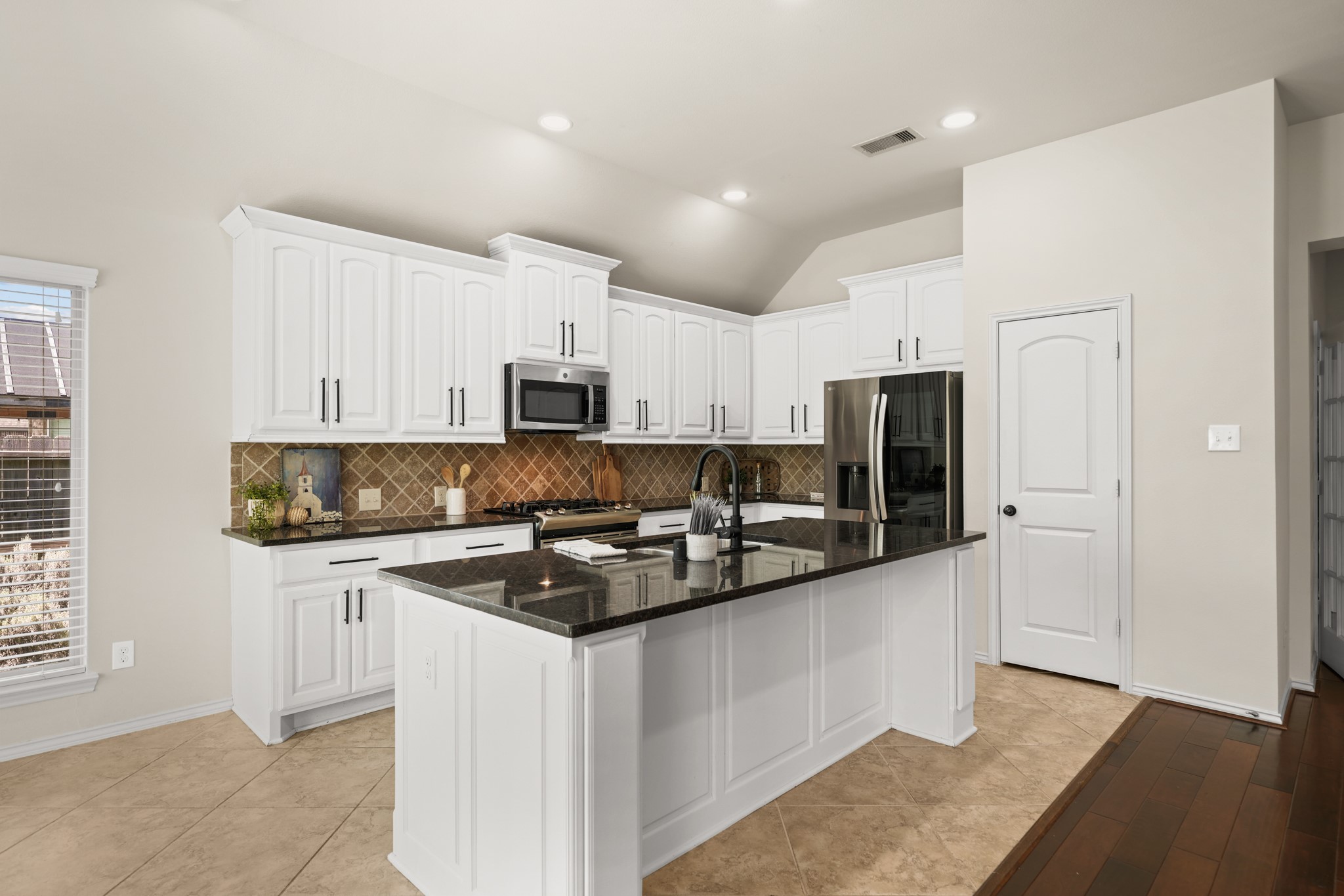 Chef-inspired kitchen with abundant cabinetry, granite countertops, stainless steel appliances, gas cooktop, and oversized island.