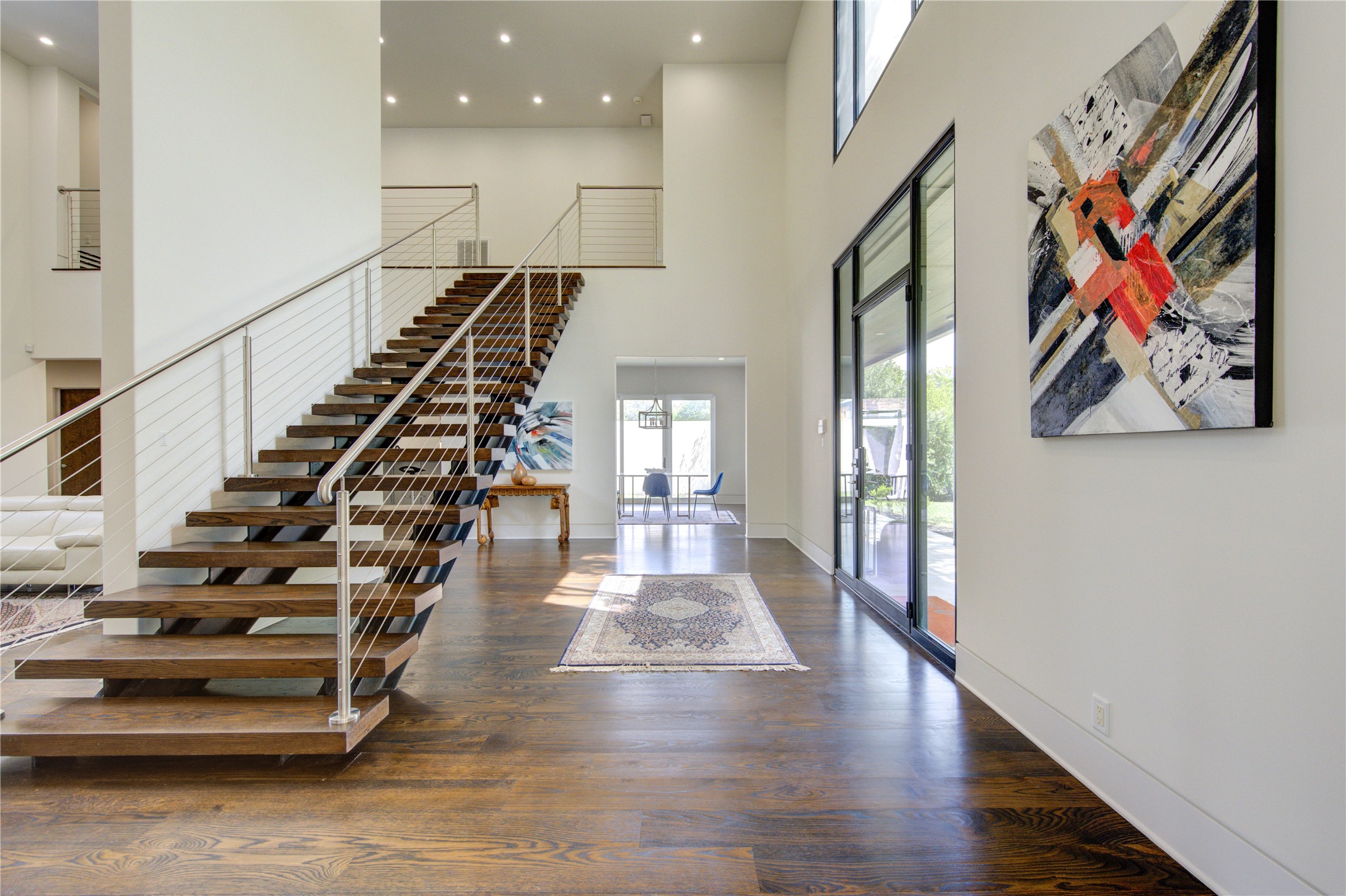 This modern home features an open, airy foyer with high ceilings and a sleek floating staircase. Large windows provide plenty of natural light, while contemporary artwork and hardwood floors add elegance.