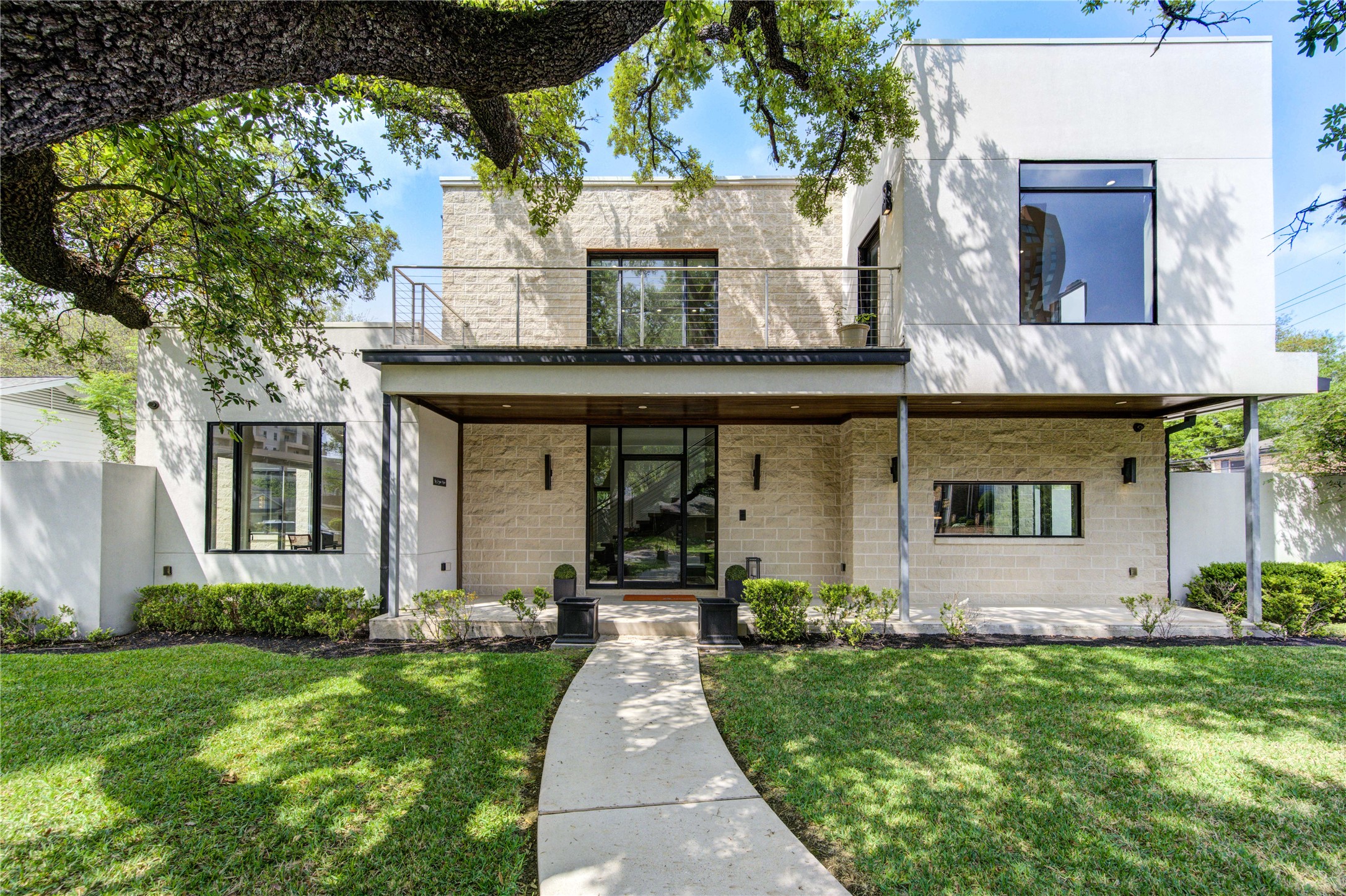 A sleek facade with large windows, a clean white exterior, and stone accents. The entrance is framed by a spacious porch and well-maintained landscaping, creating a welcoming atmosphere.